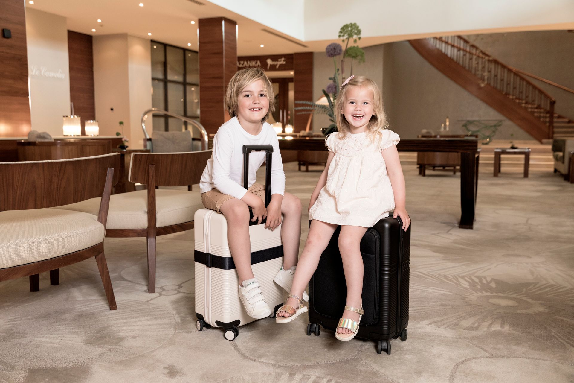 A boy and a girl are sitting on suitcases in a hotel lobby.