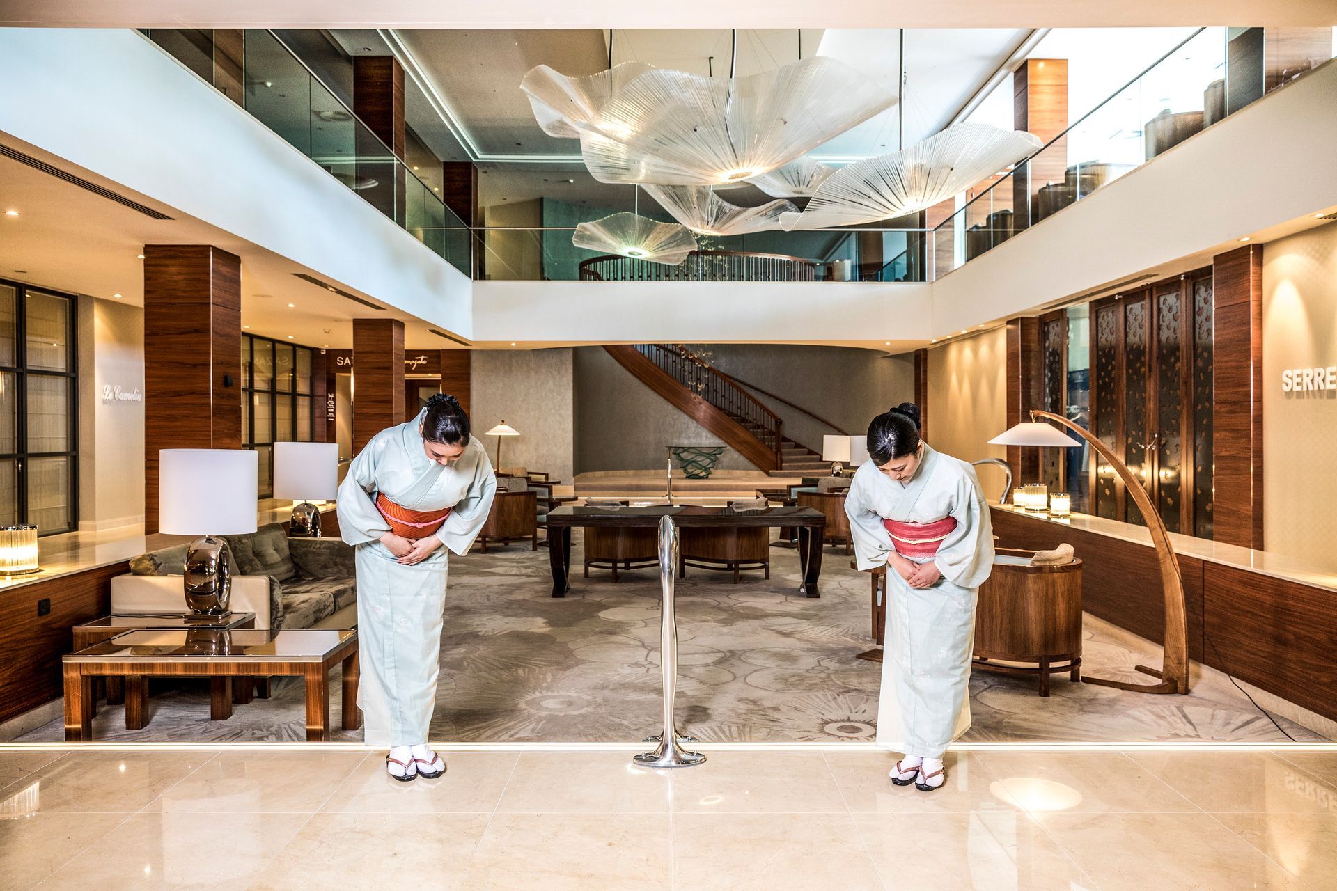 Two women in kimonos are bowing in a hotel lobby.