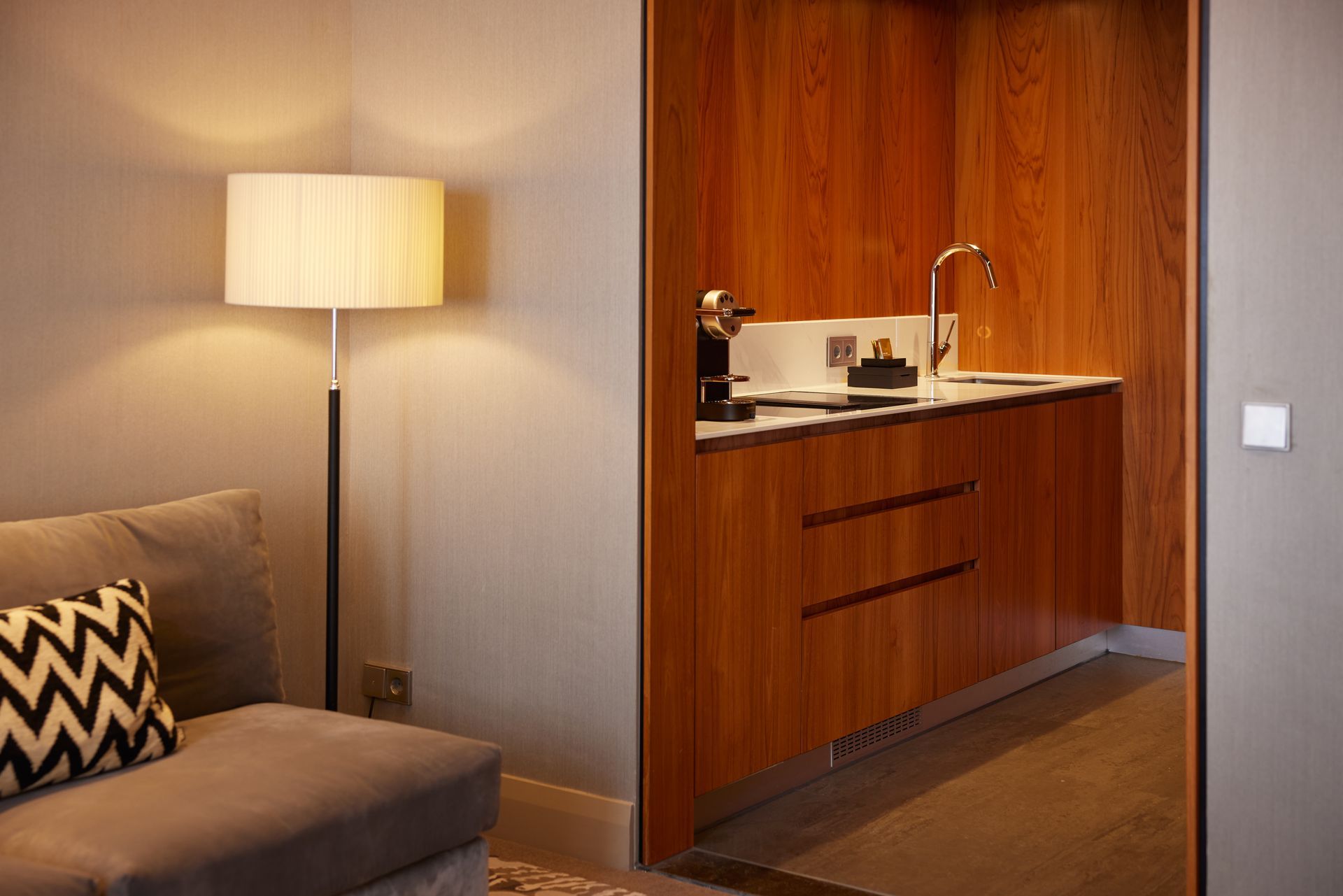 A living room with a couch and a lamp next to a kitchen.