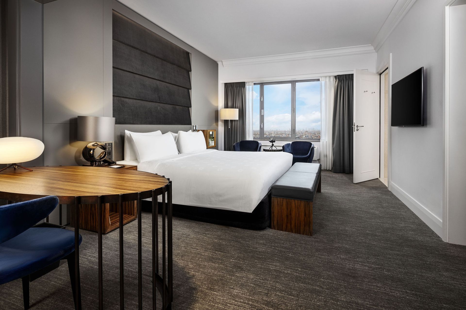 A hotel room with a king size bed , table , chairs and television.