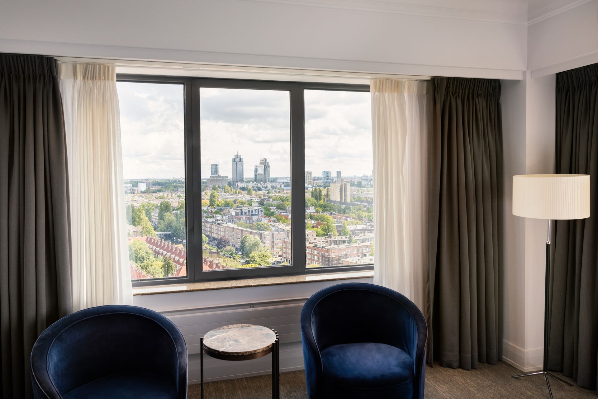 A hotel room with two chairs and a large window with a view of the city.