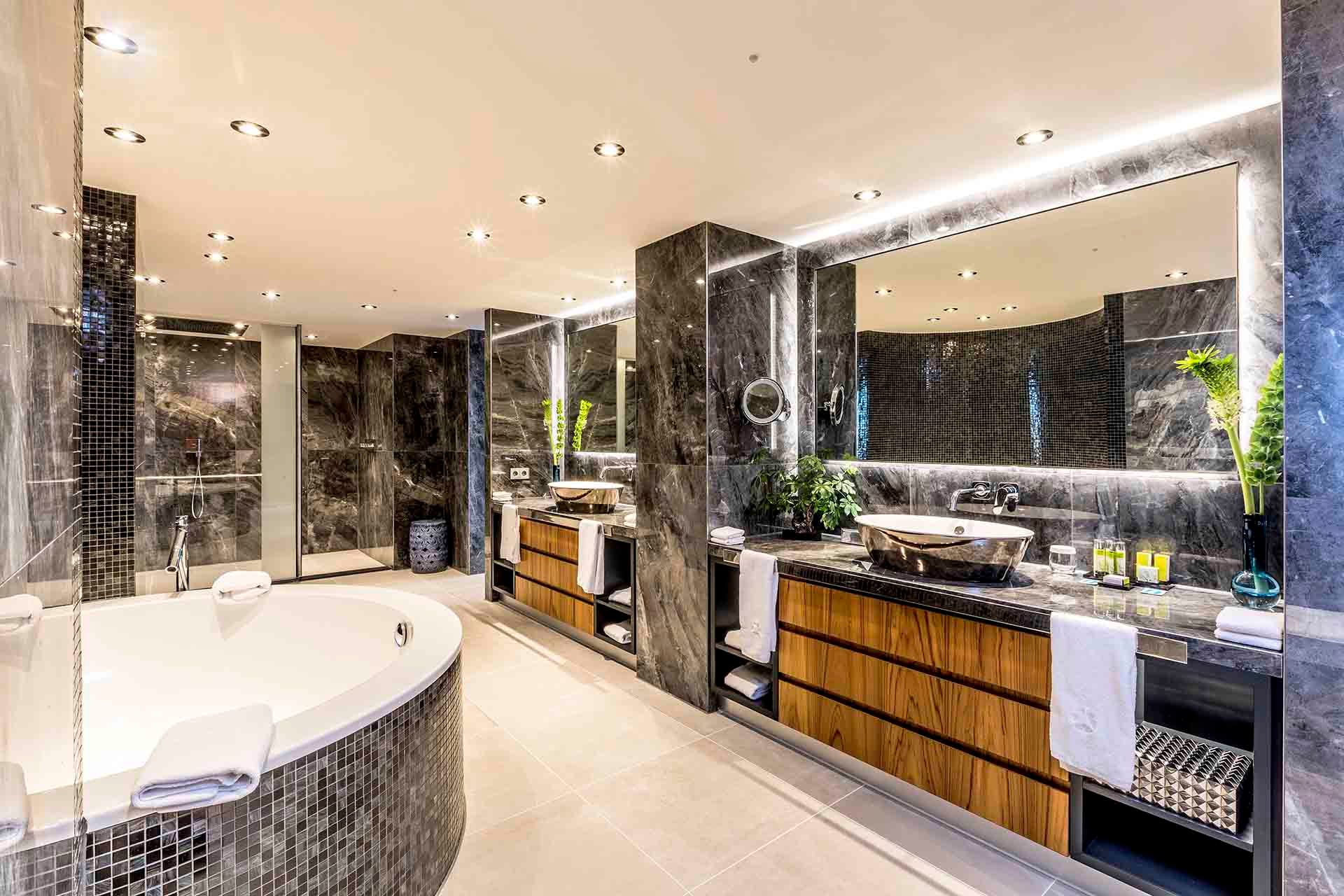 A bathroom with two sinks , a tub , and a large mirror.