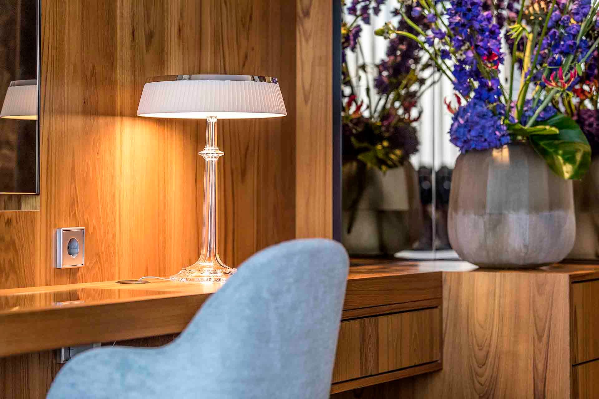 A lamp is sitting on a wooden desk next to a chair.