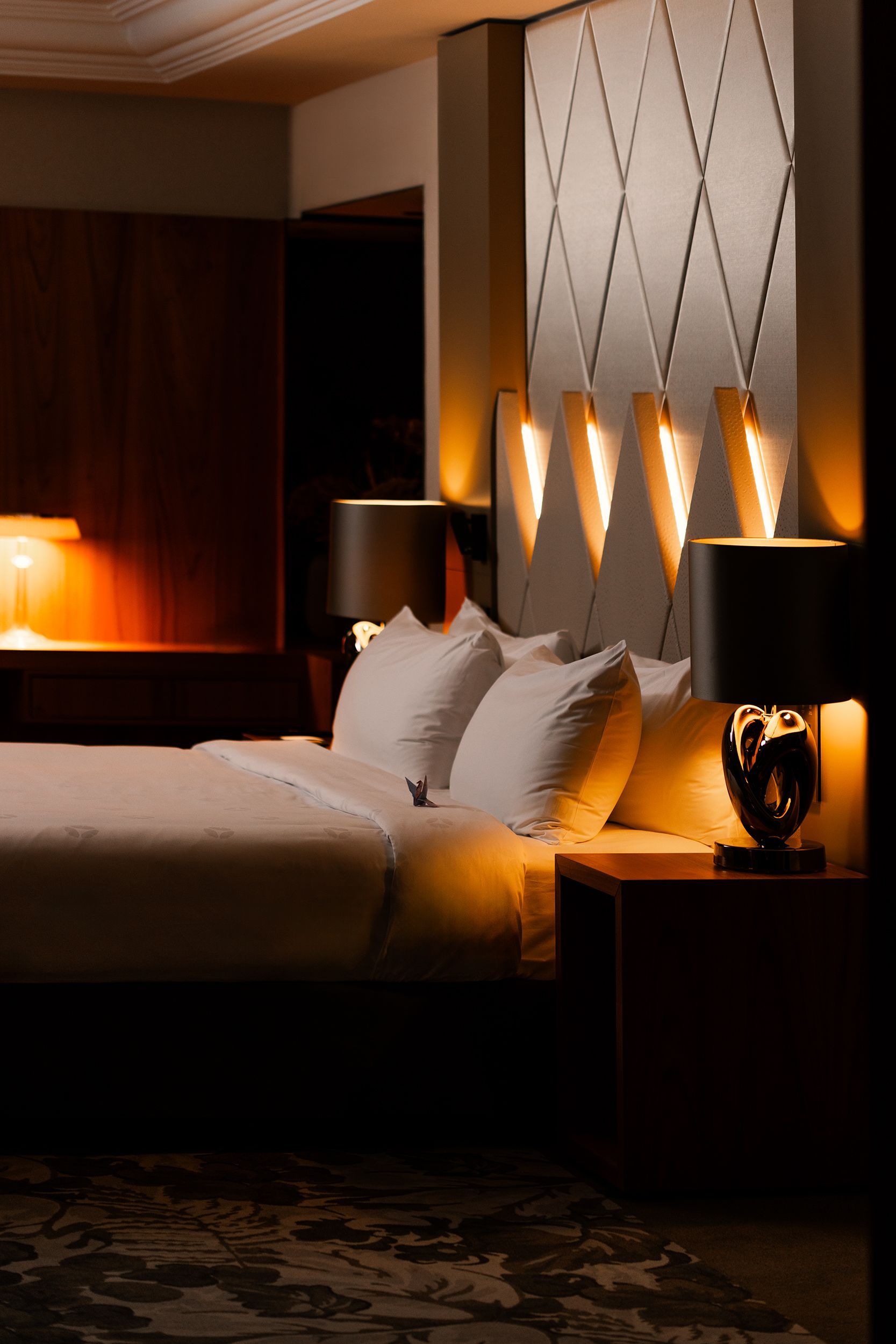 A hotel room with a bed , lamps and a nightstand.