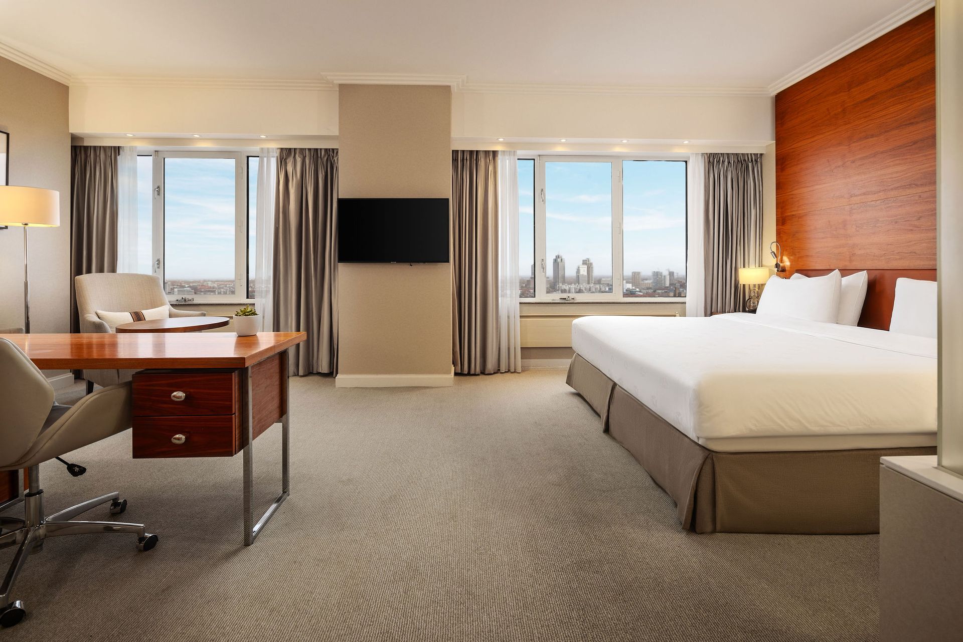 A hotel room with a king size bed , desk , chair and television.