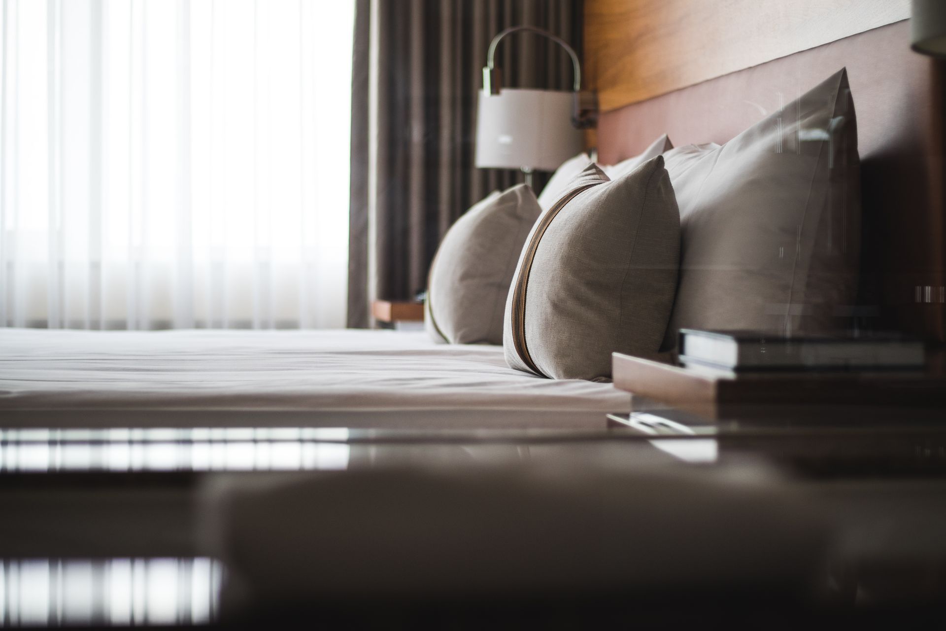 A hotel room with a bed , pillows , lamps and a window.