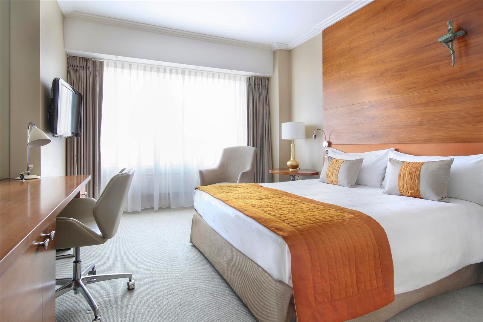 A hotel room with a king size bed , desk , chair and television.