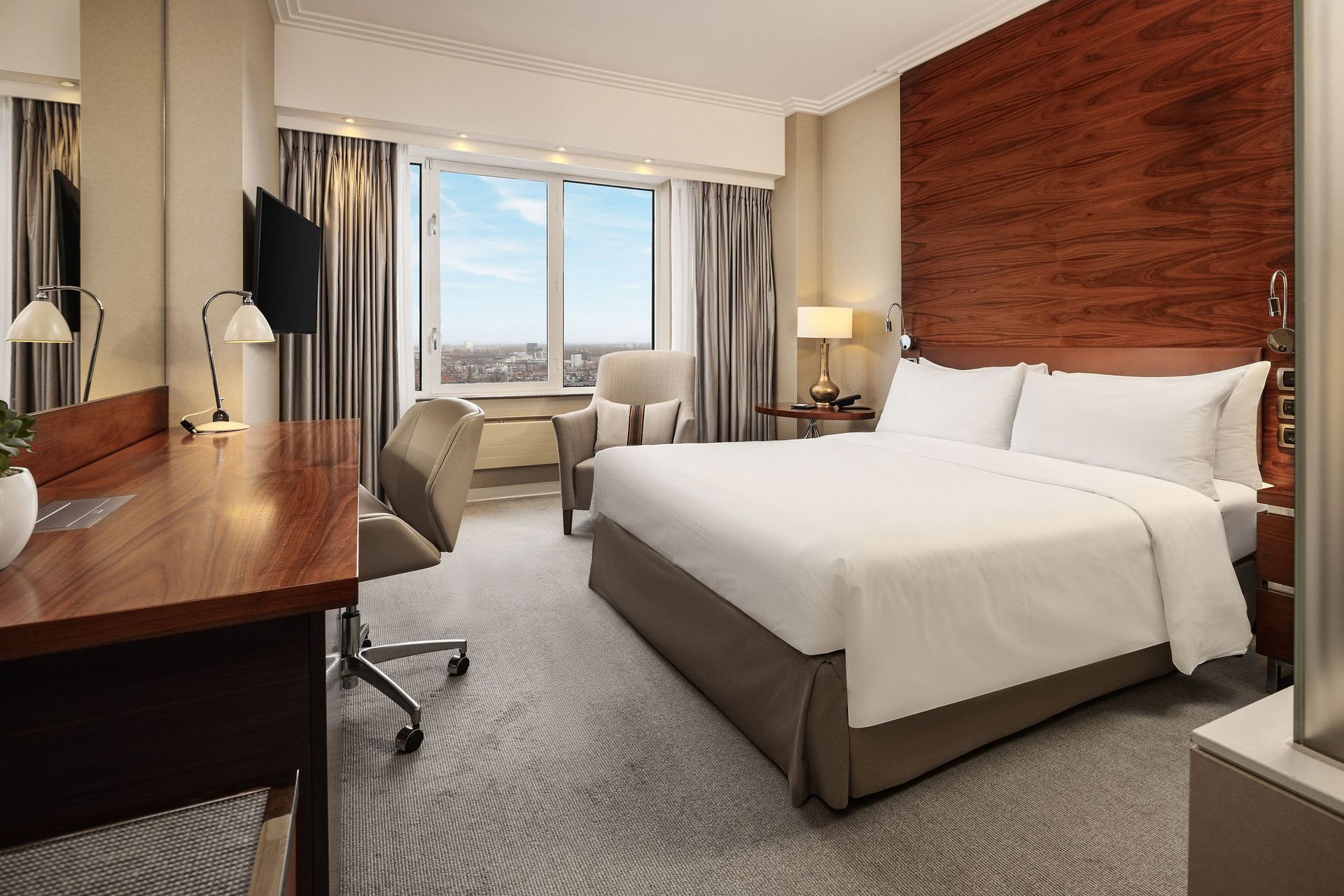 A hotel room with a king size bed , desk , chair and television.