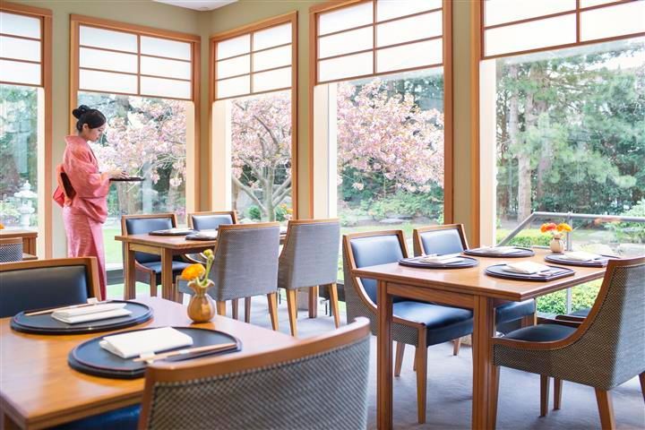 Een vrouw in een kimono serveert eten in een restaurant met tafels en stoelen.