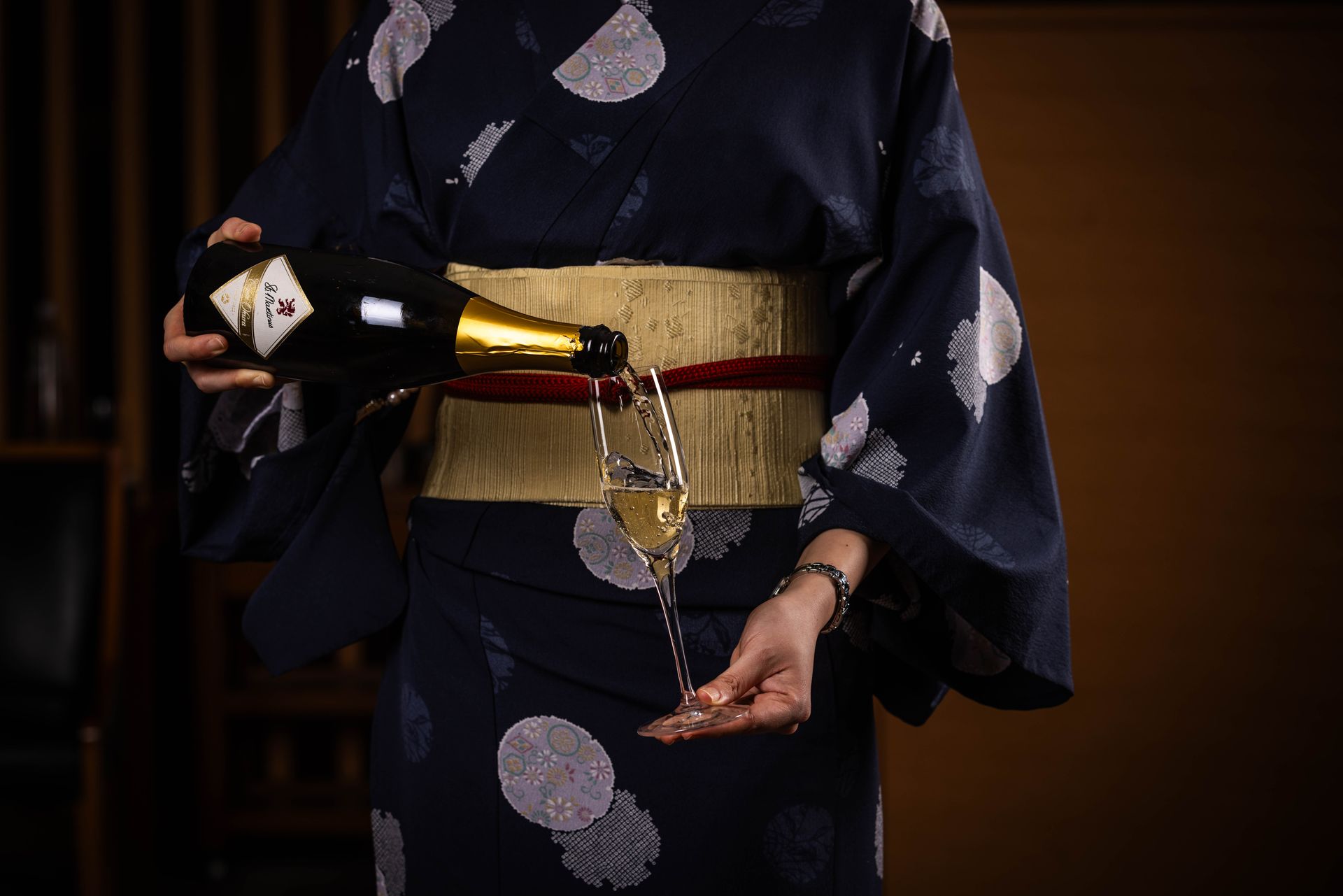 A woman in a kimono is pouring champagne into a glass.