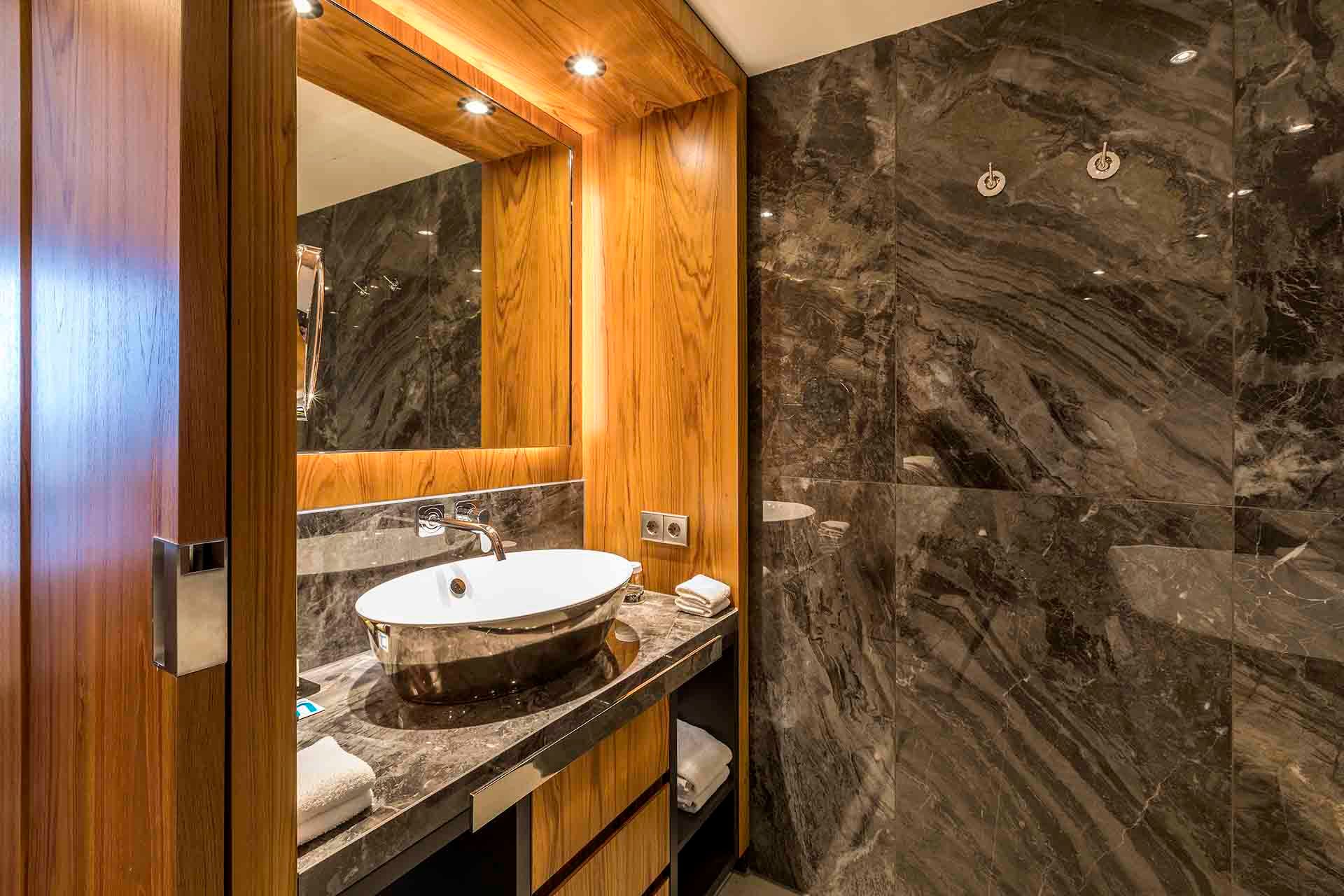 A bathroom with a sink , mirror and marble wall.