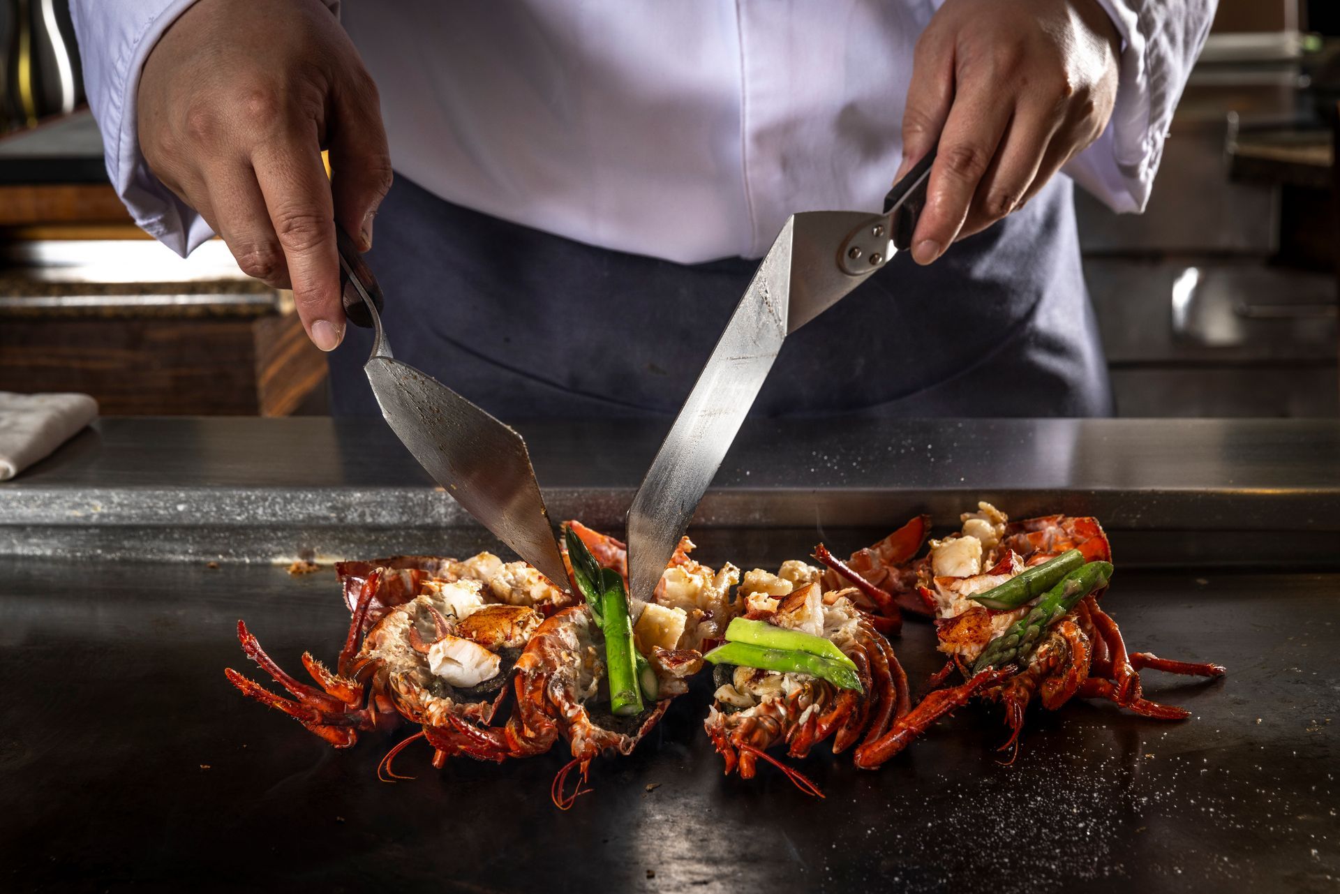 Chef grilling lobster and vegetables on a teppanyaki grill.