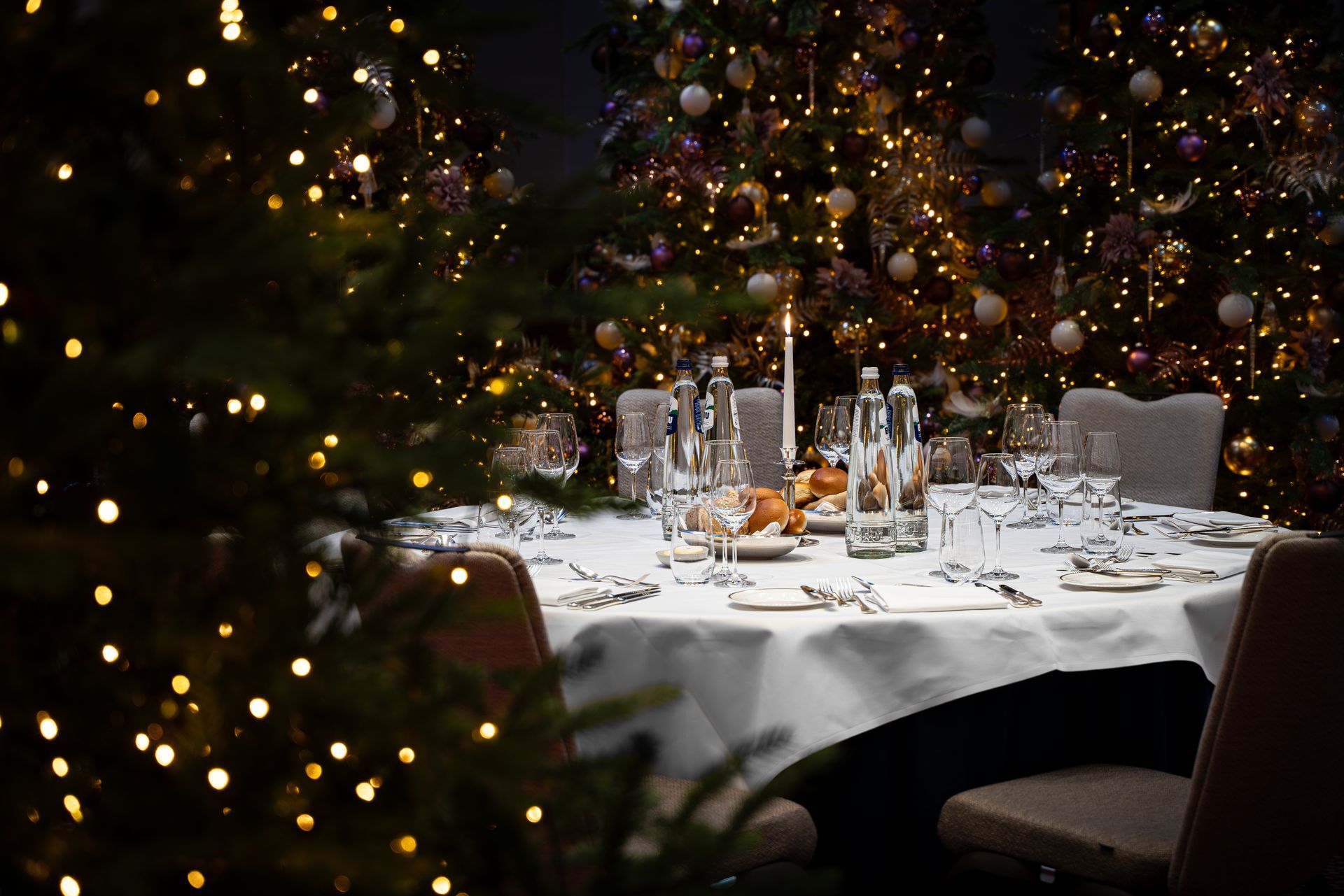 Een feestelijk gedekte eettafel voor een feestmaaltijd, omringd door versierde kerstbomen en zachte lampjes.