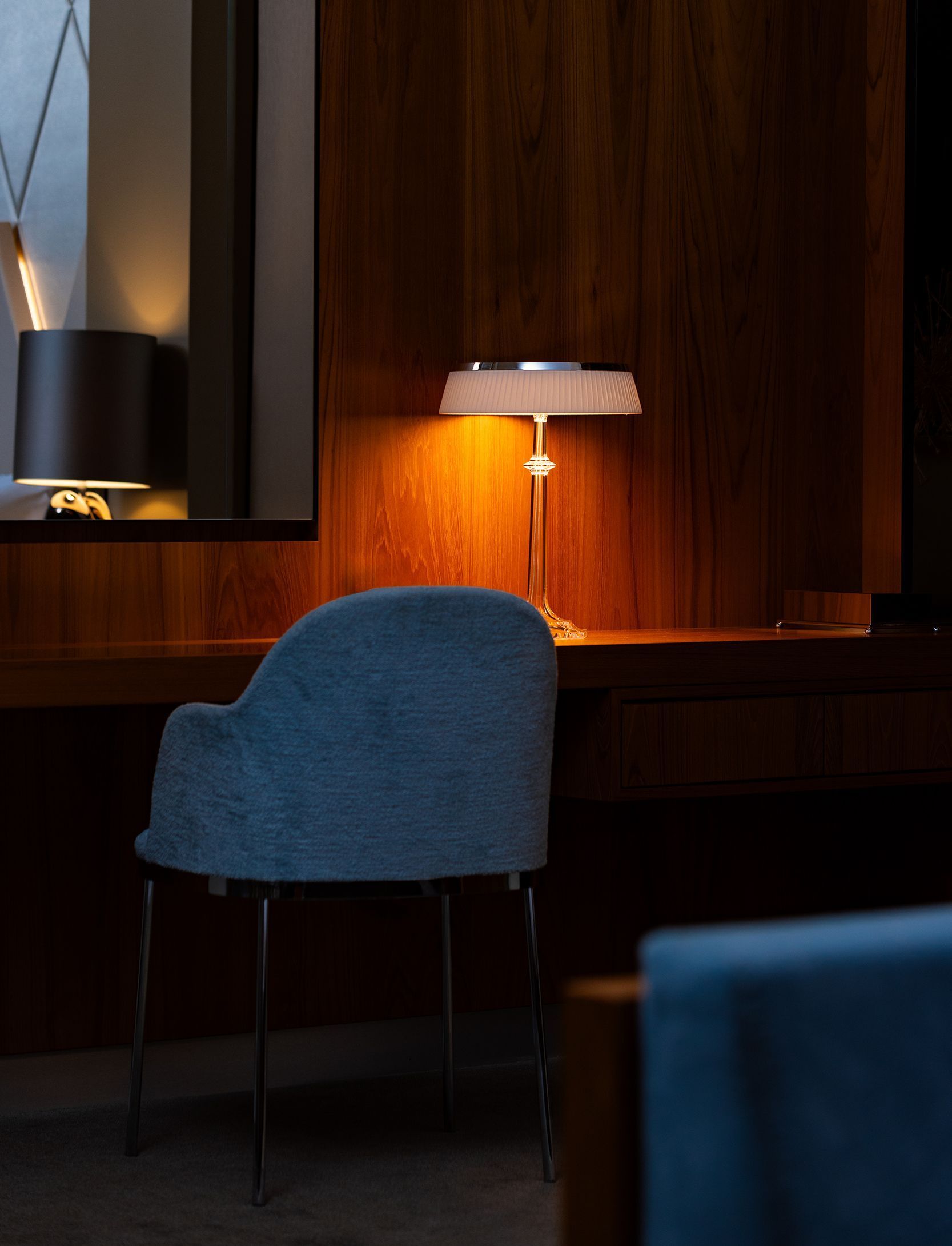 A chair is sitting in front of a desk with a lamp on it.