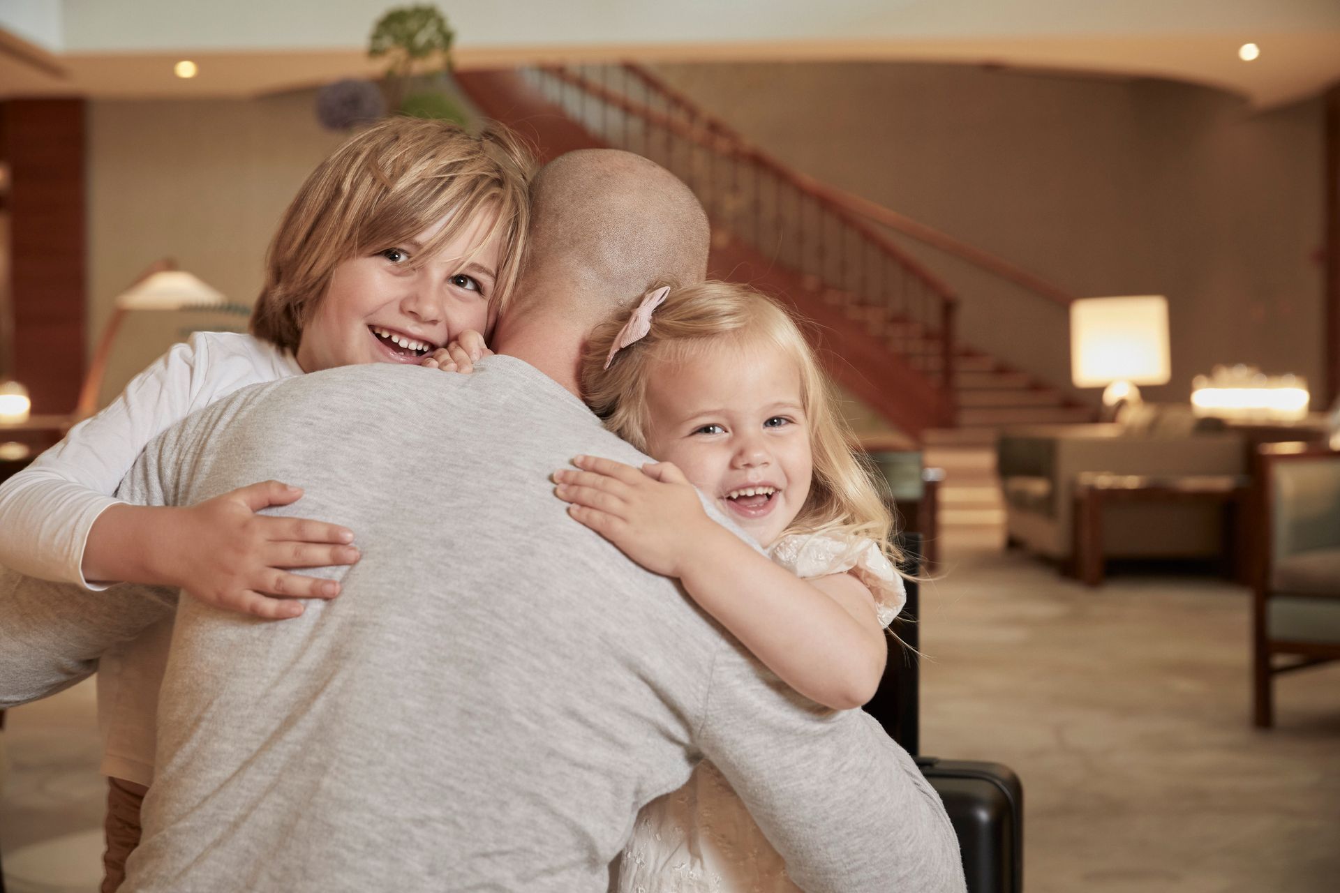 A man is hugging two little girls in a hotel lobby.