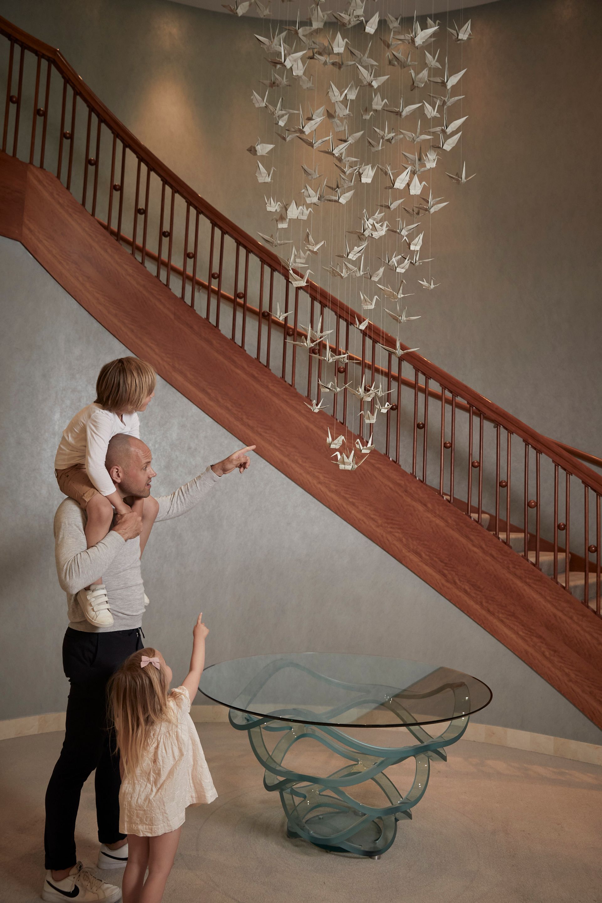 A man and two children are standing on a staircase looking at a chandelier.