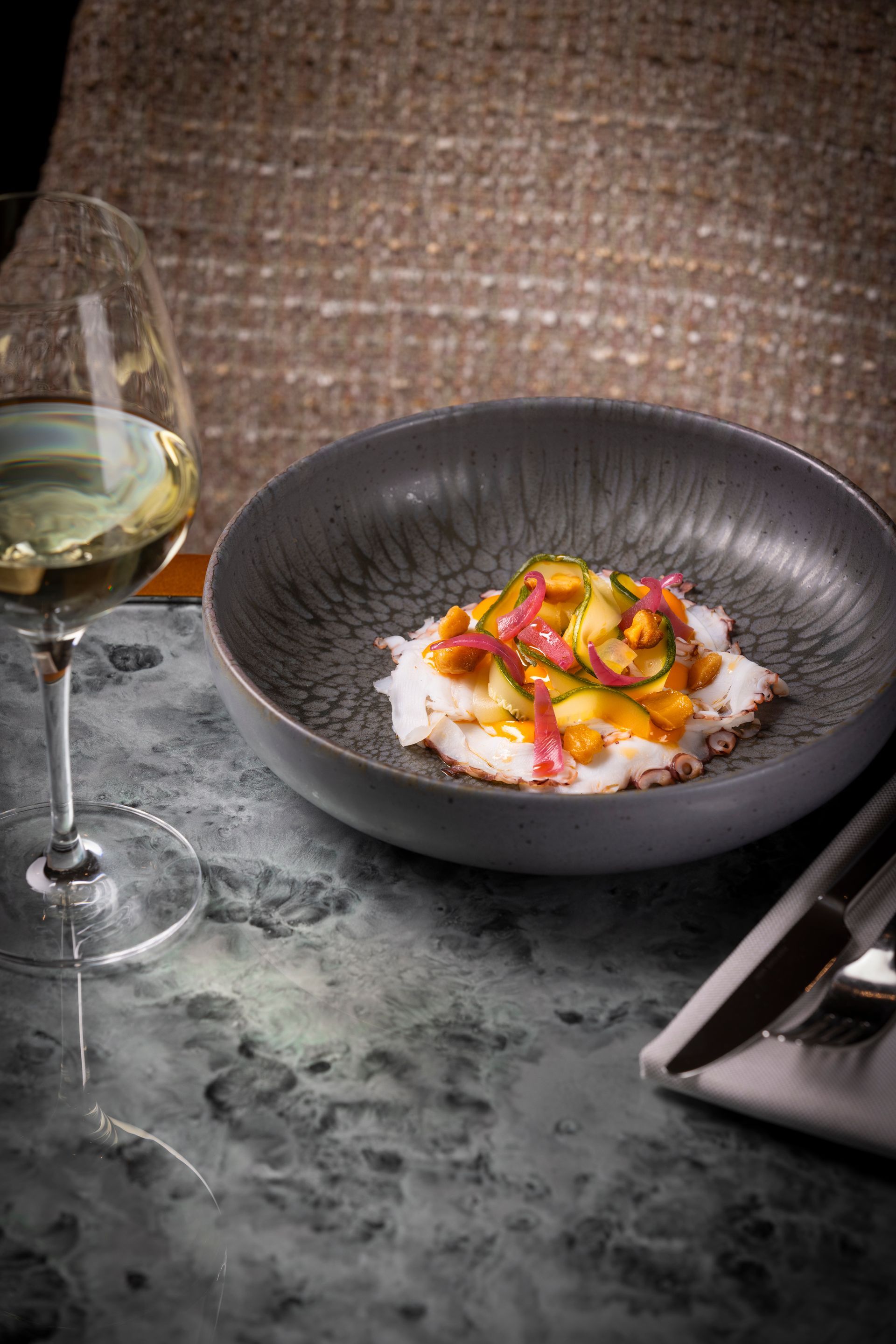 A bowl of food and a glass of wine on a table.