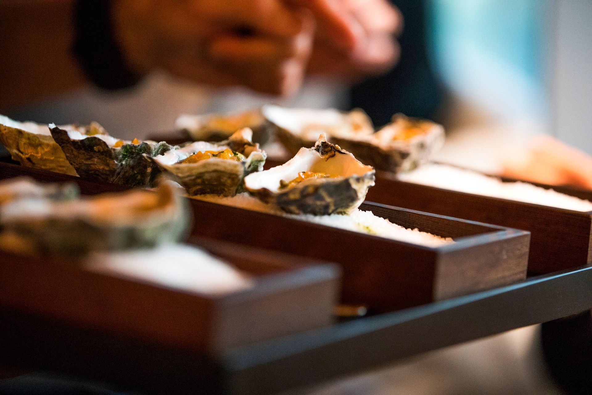 A person is eating oysters on a wooden tray.