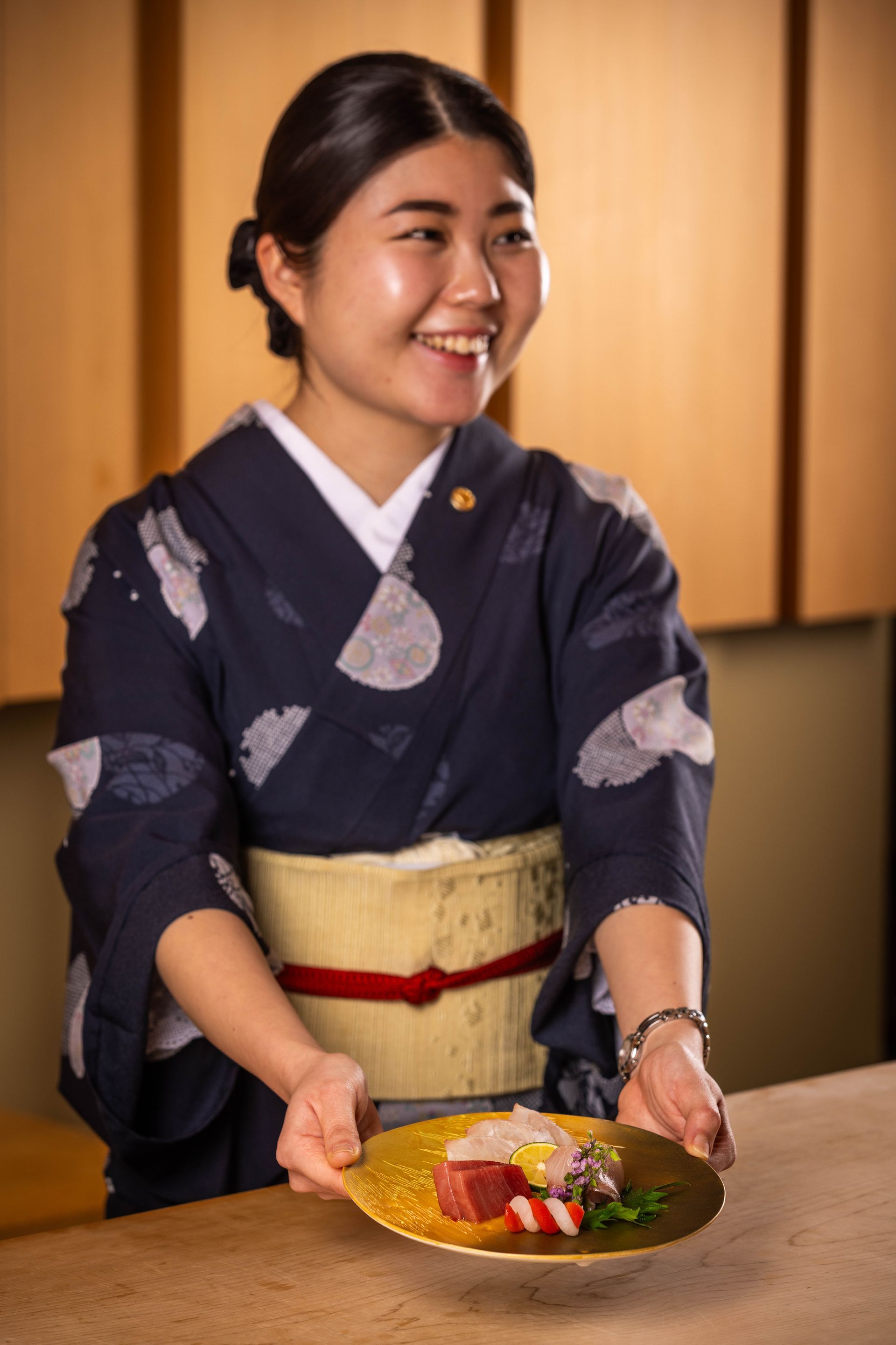 A woman in a kimono is holding a plate of food.