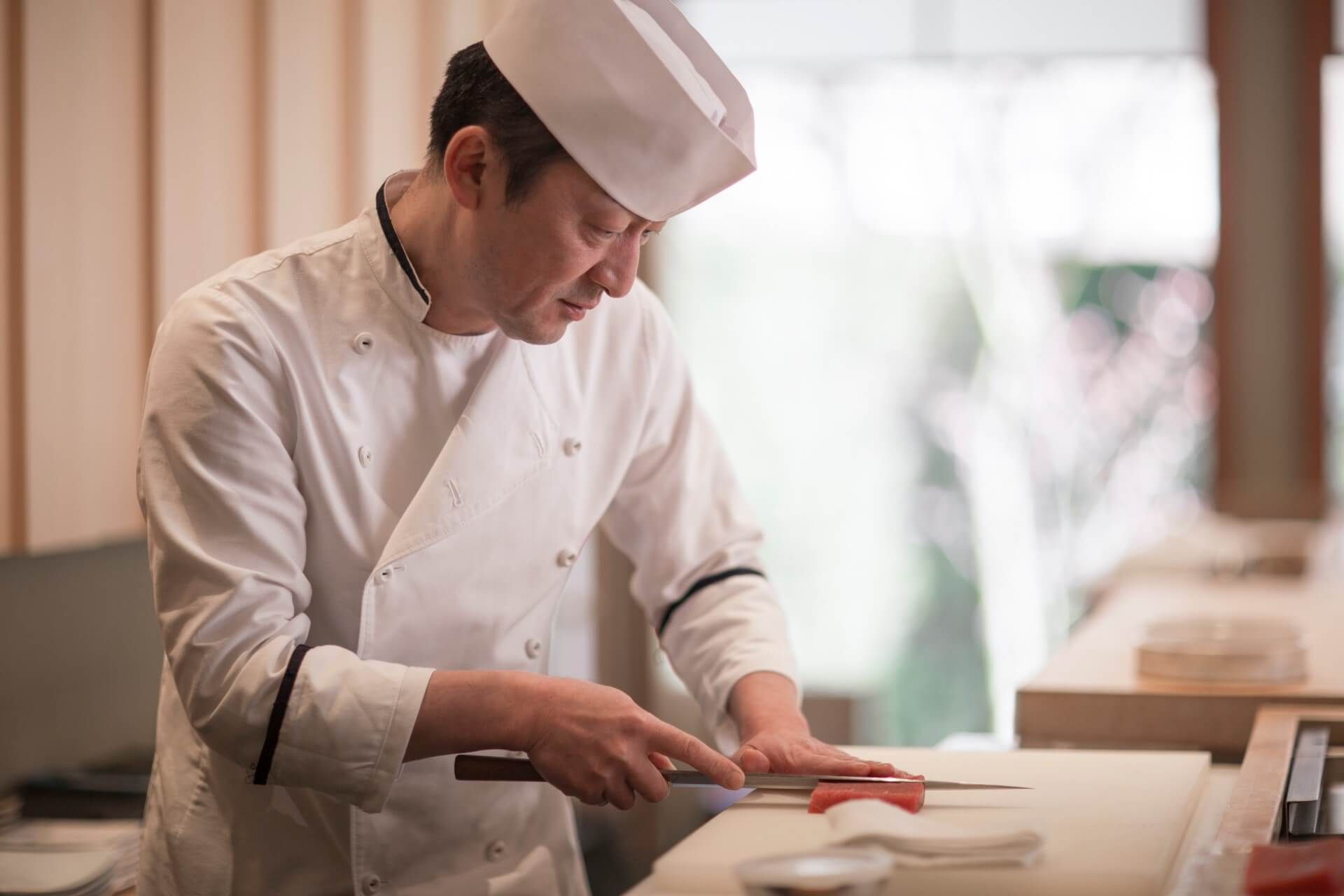 A chef is cutting a piece of meat on a cutting board.