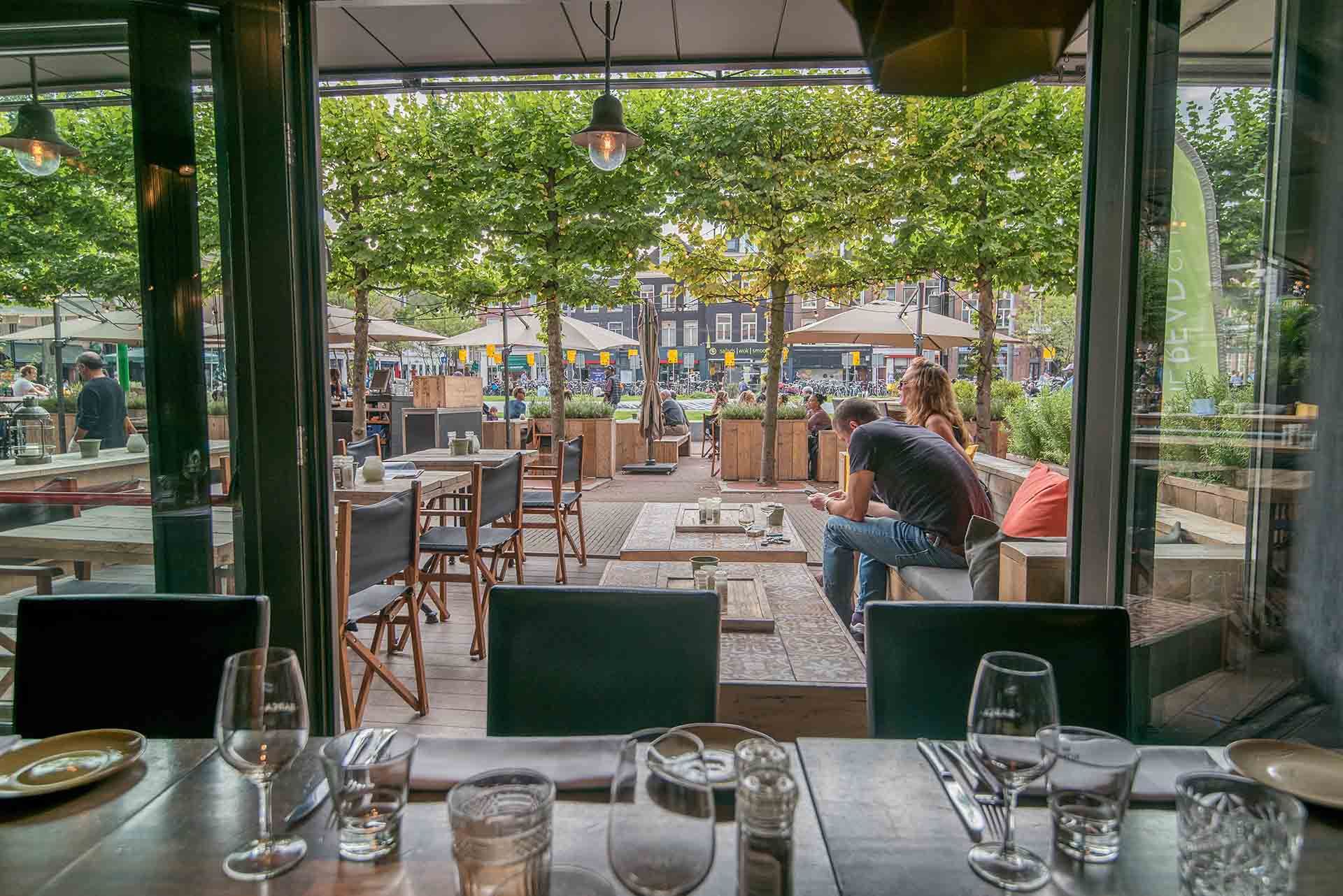 A restaurant with a lot of tables and chairs and a man sitting on a couch.