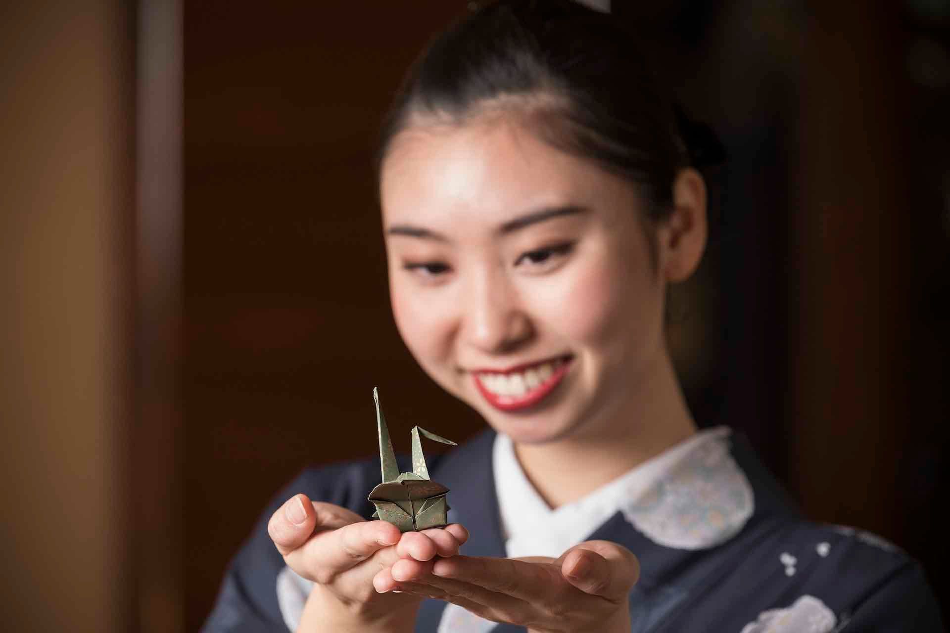 A woman in a kimono is holding a small origami crane in her hands.