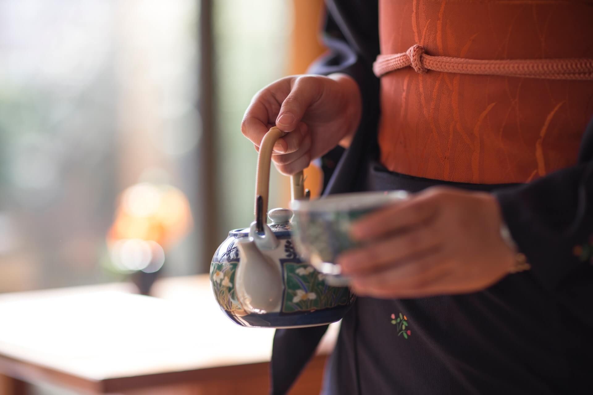 A person is holding a teapot and a cup of tea.