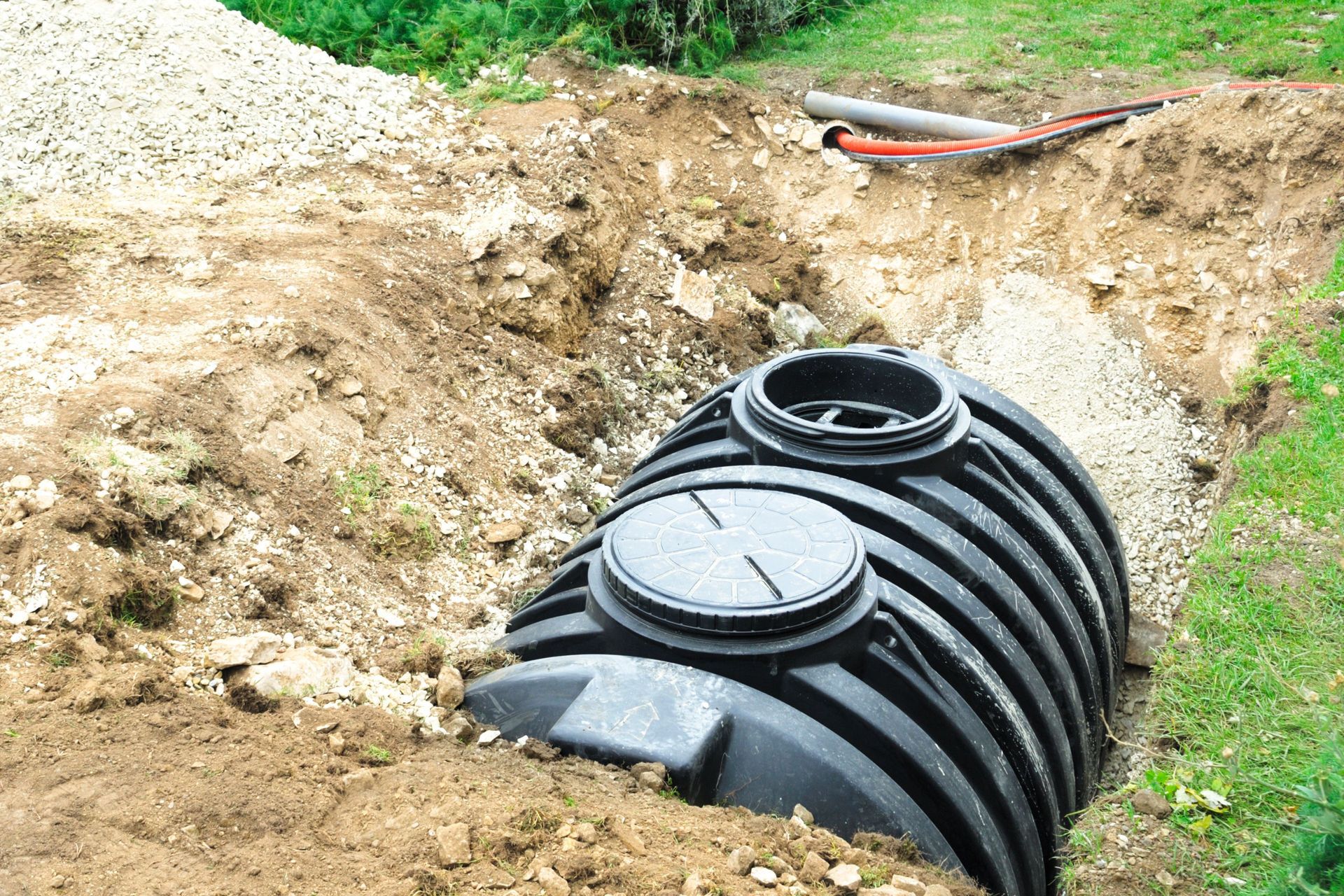 Black plastic septic tank installed in an open dirt trench at a construction site