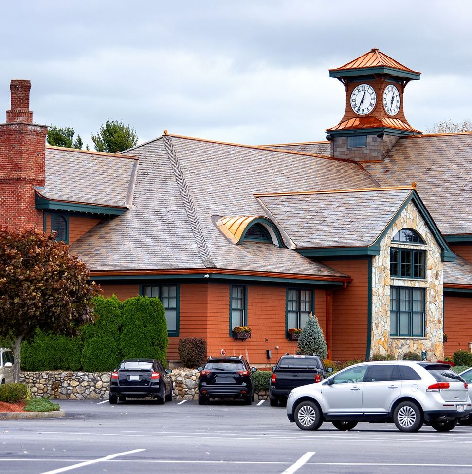 Building with clock tower, copper roof, stone facade, and parked cars in a parking lot.
