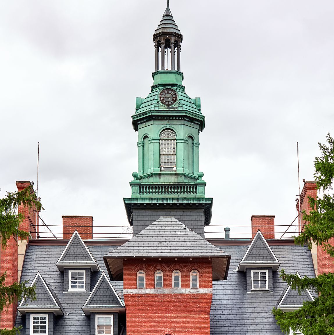 Copper-topped tower with clock atop a red brick building with a slate roof.