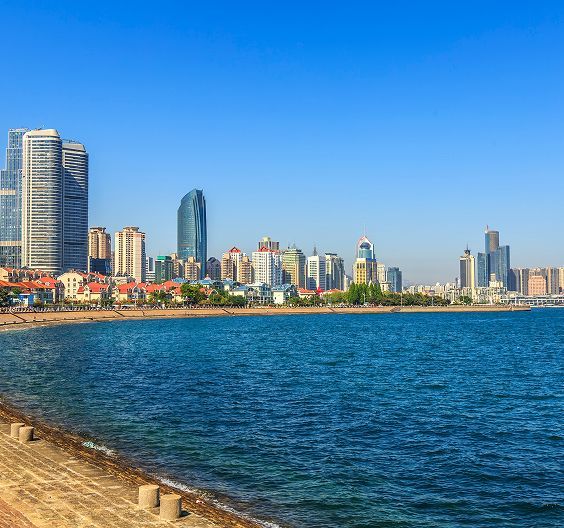 Coastal city skyline with tall buildings, sandy beach, and blue water under a clear sky.