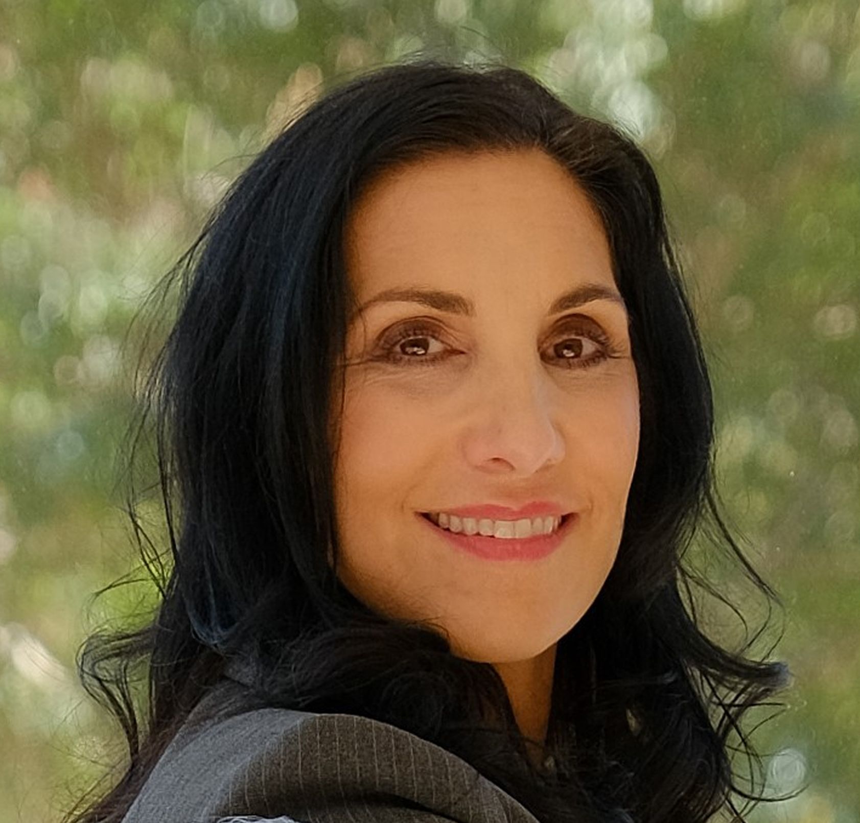 Woman in a black blazer smiles with arms crossed in front of a house.