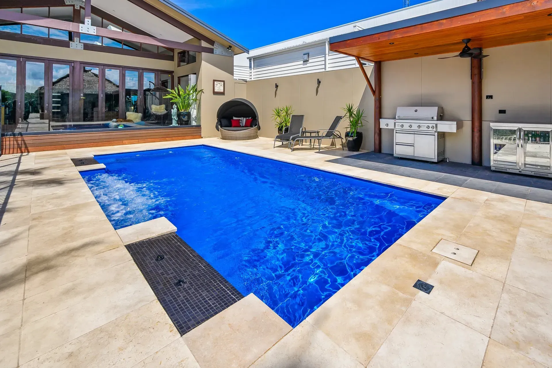 A large swimming pool is surrounded by a patio and a grill.