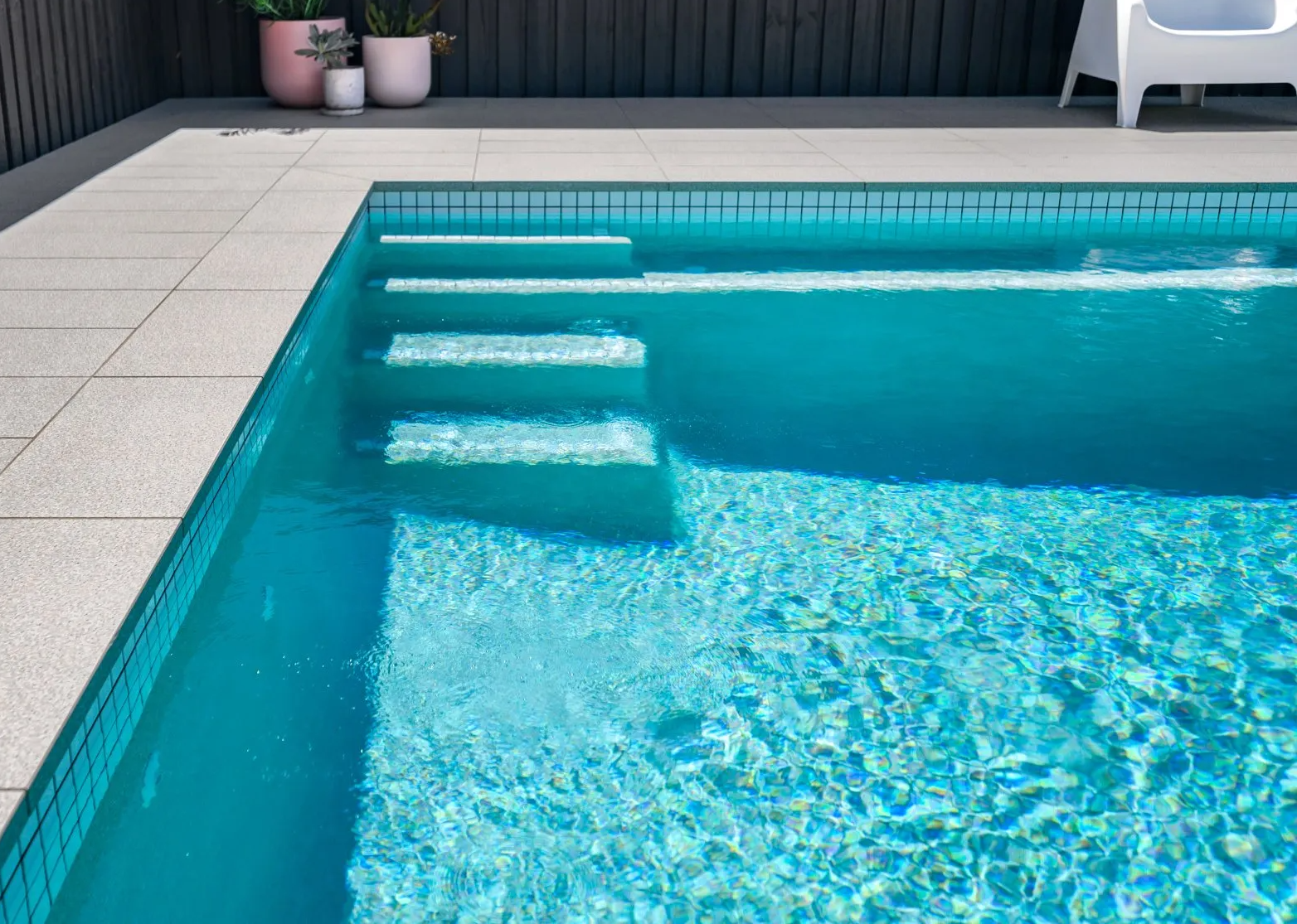 A swimming pool with stairs and a chair in the background.