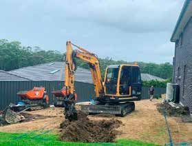 A small excavator is digging a hole in the ground in front of a house.