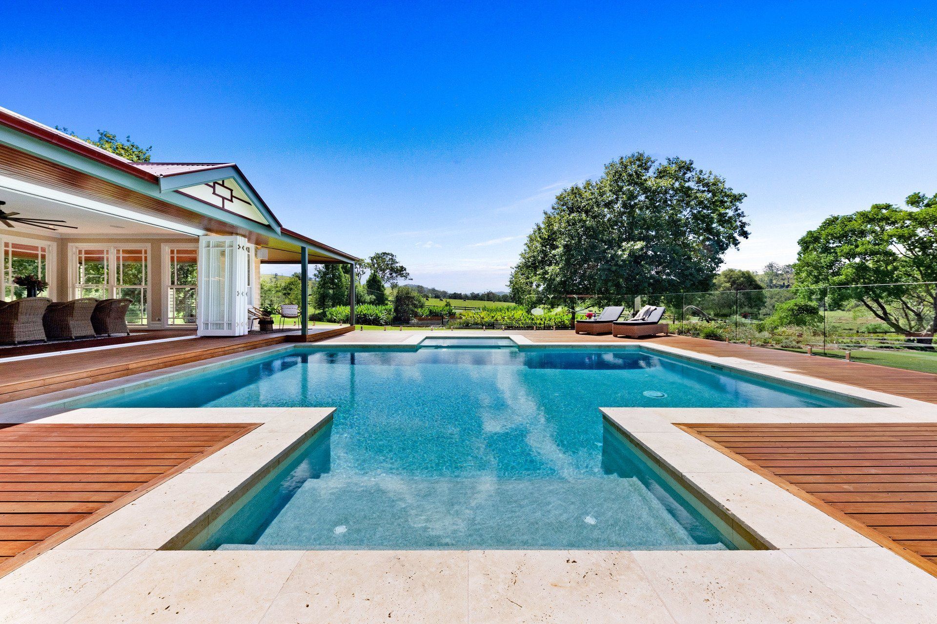A large swimming pool with a wooden deck in front of a house.