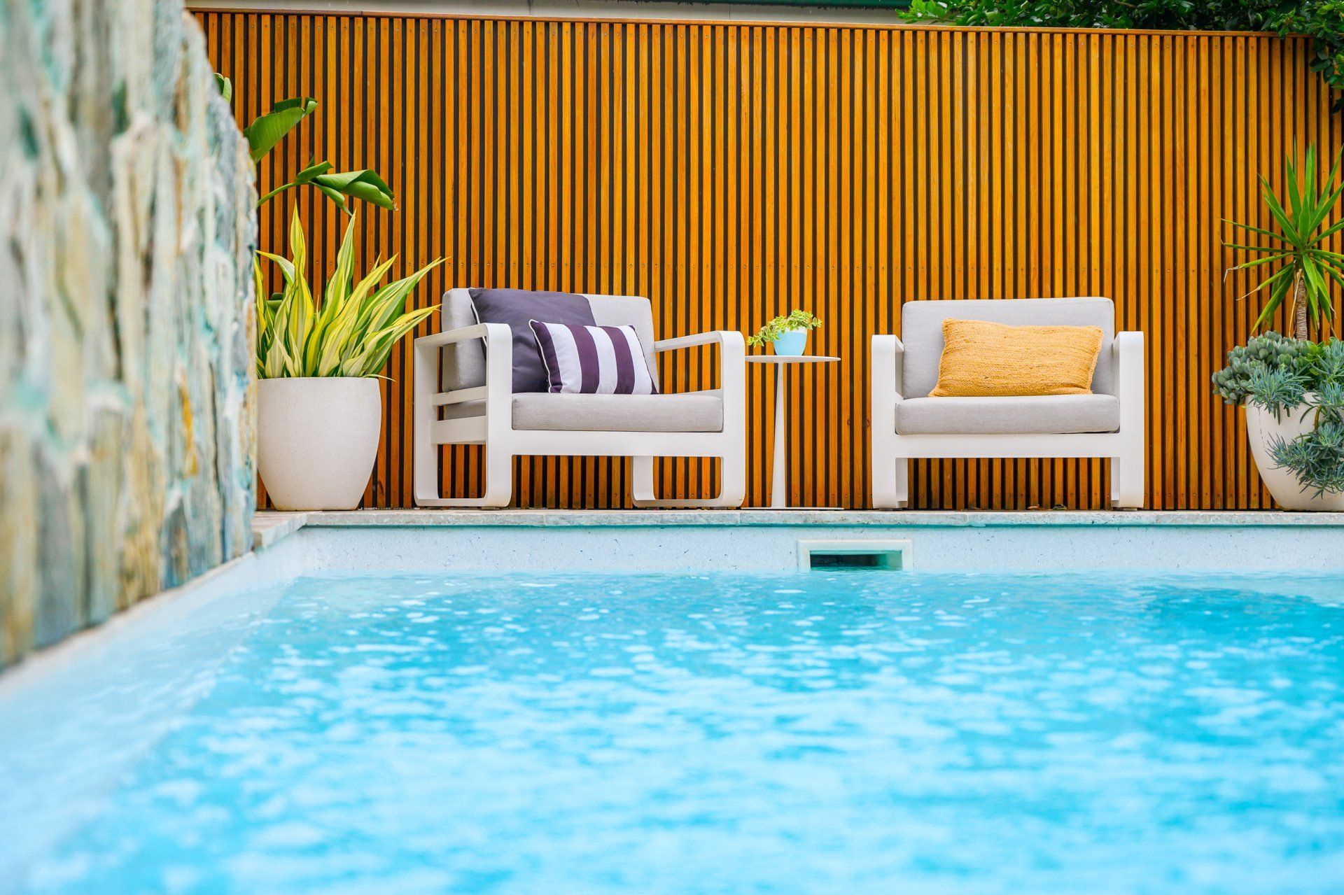 A swimming pool with two chairs and a table next to it.