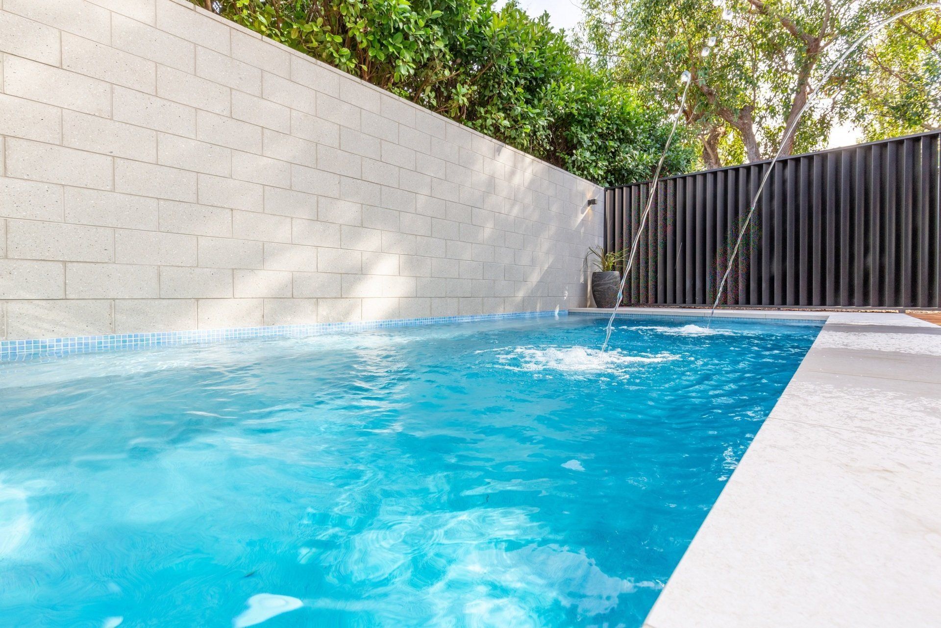 A large swimming pool surrounded by a white brick wall and a black fence.