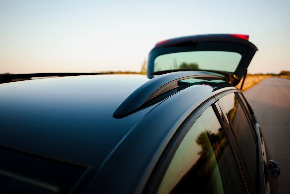 A close-up of a car with tinted windows parked on a quiet road under the sun.