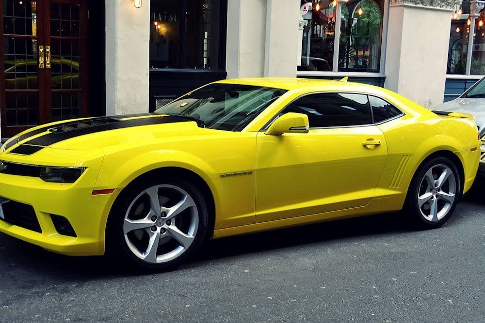 A yellow Chevrolet Camaro with dark-tinted windows parked in front of a building.