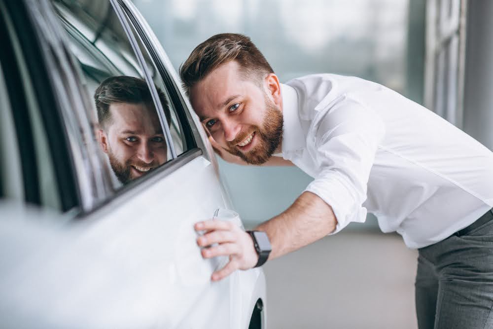 A man inspecting a car window for signs of window tint bubbles.
