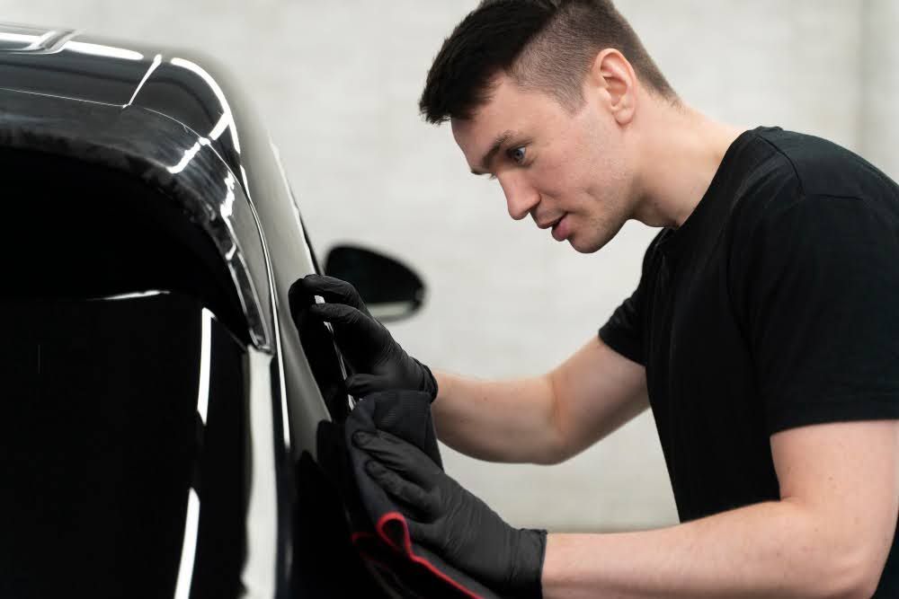 A professional applying ceramic tint film to a car window.