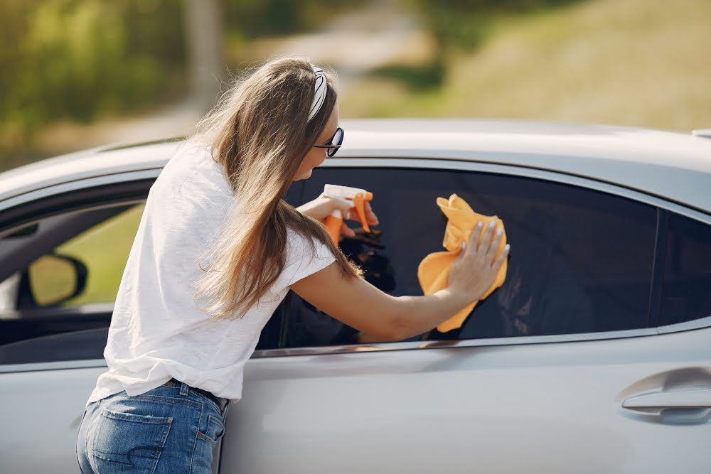 A woman wiping a car window with ceramic tint applied.