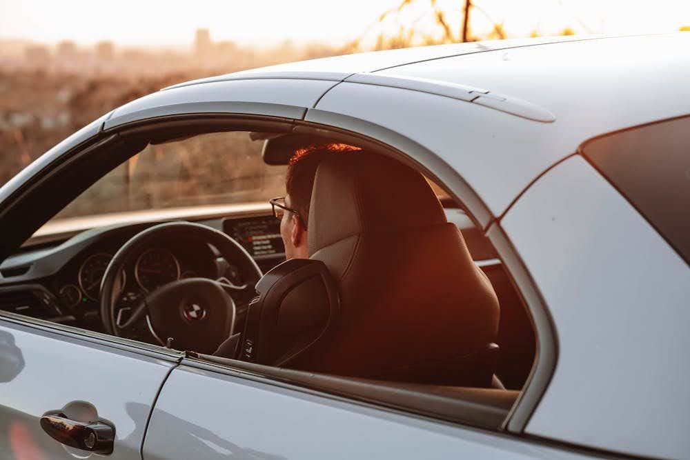 A man driving a car on a sunny, late afternoon day.
