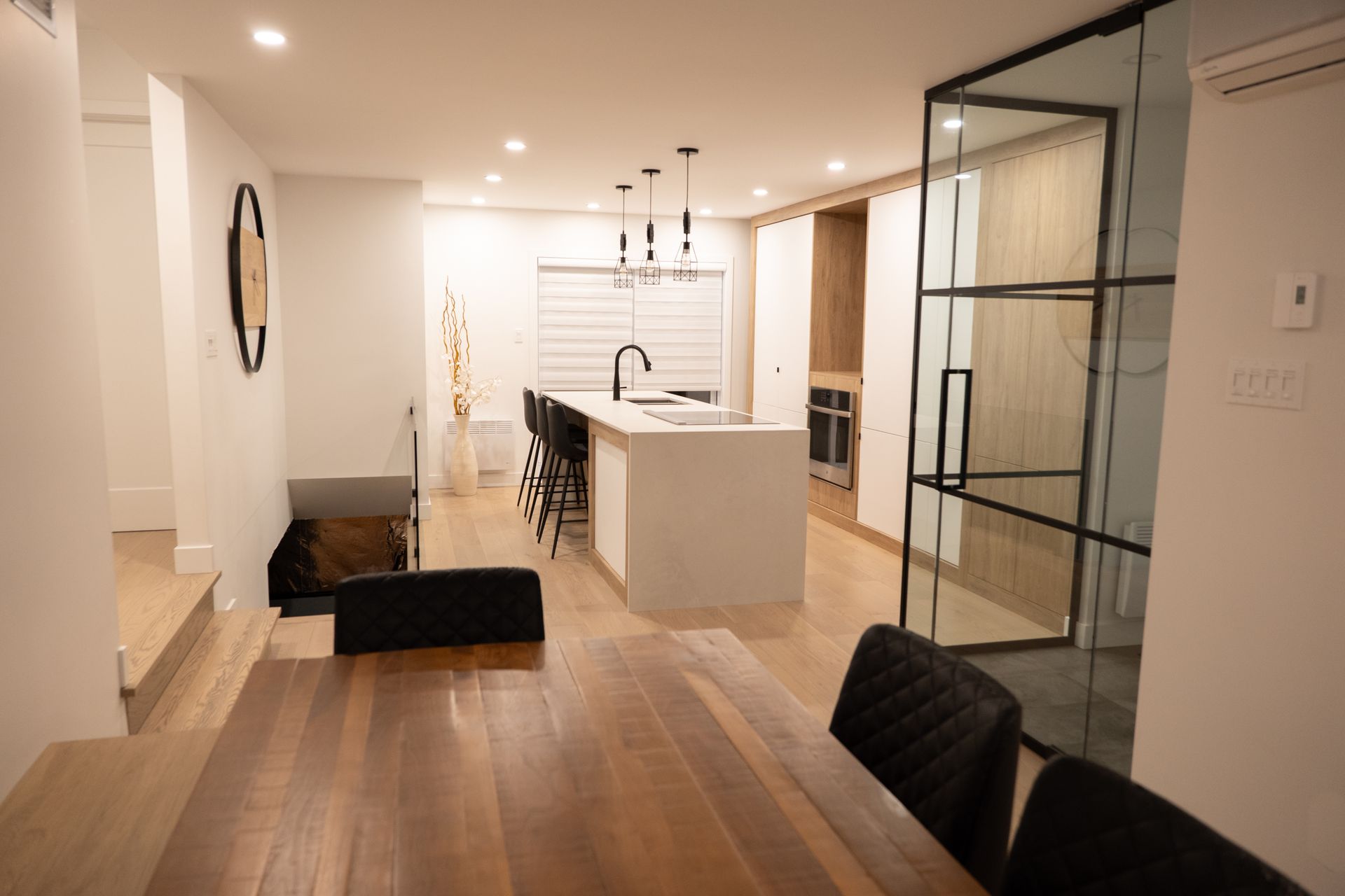 Une salle à manger avec une table et des chaises en bois et une cuisine en arrière-plan.