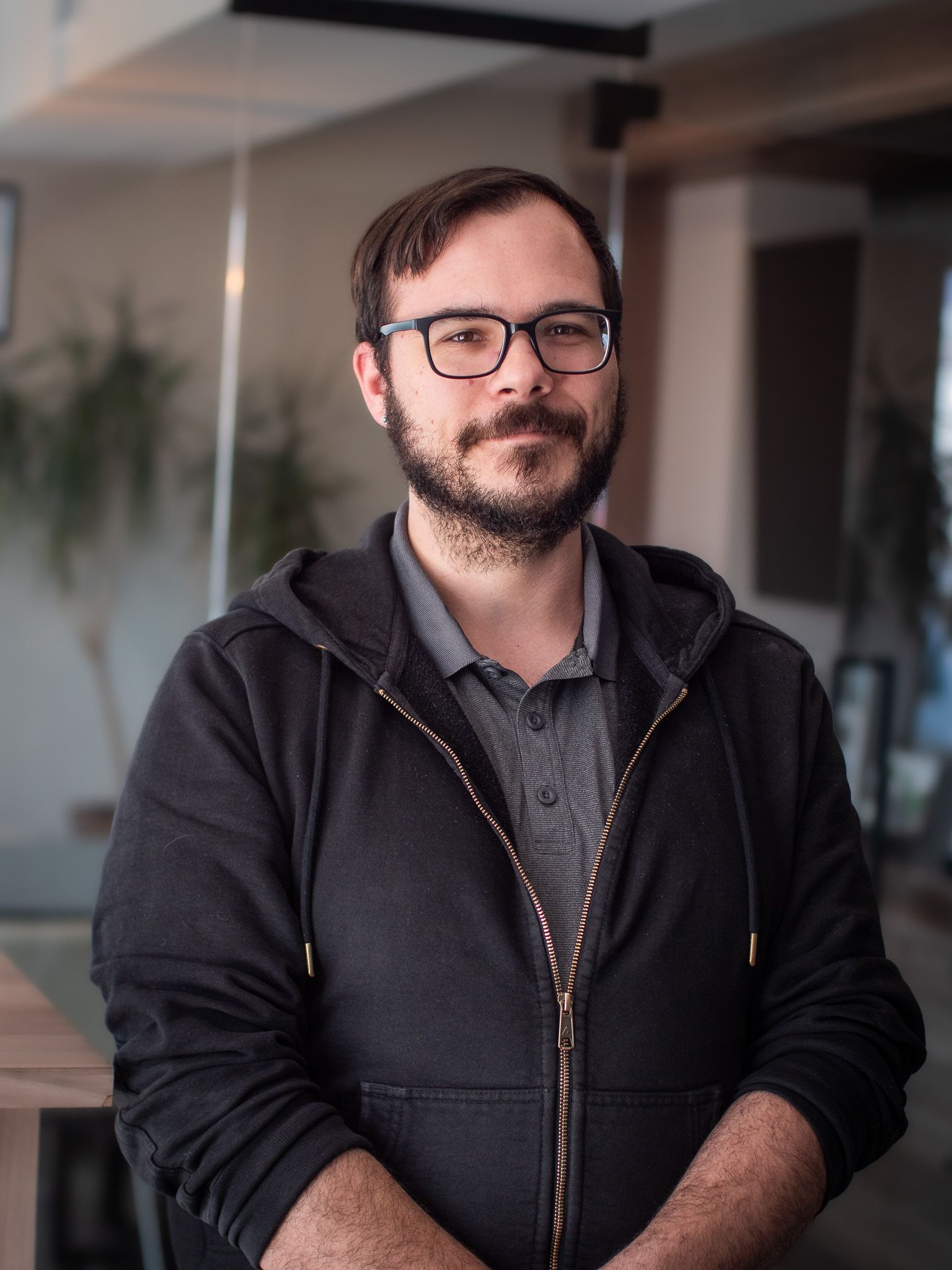 Un homme avec une barbe et des lunettes porte un sweat à capuche noir.