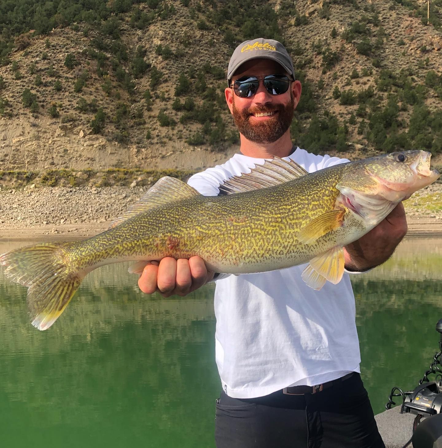 A man is holding a large fish in his hands in front of a lake.