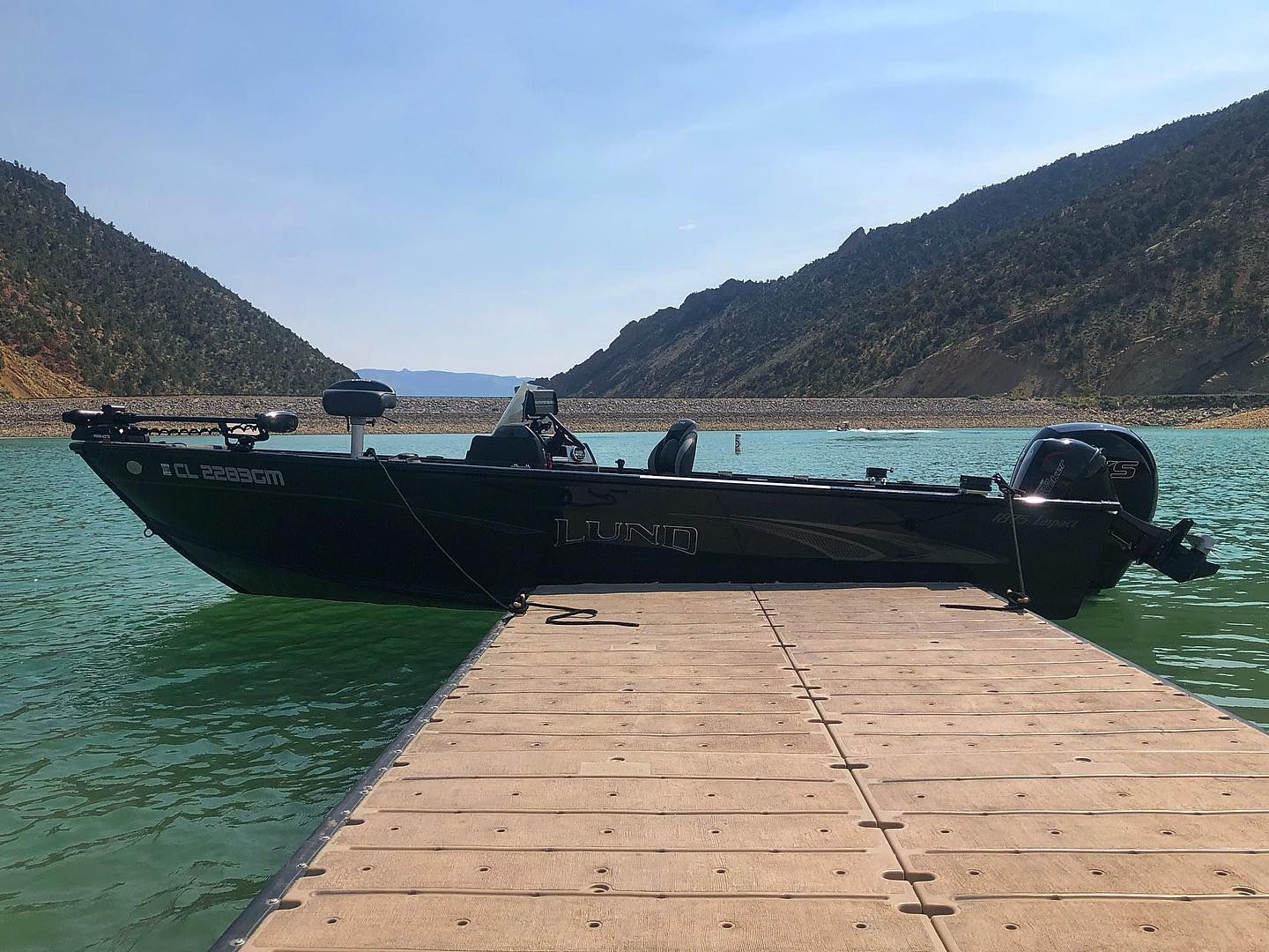 A boat is docked at a dock on a lake with mountains in the background.