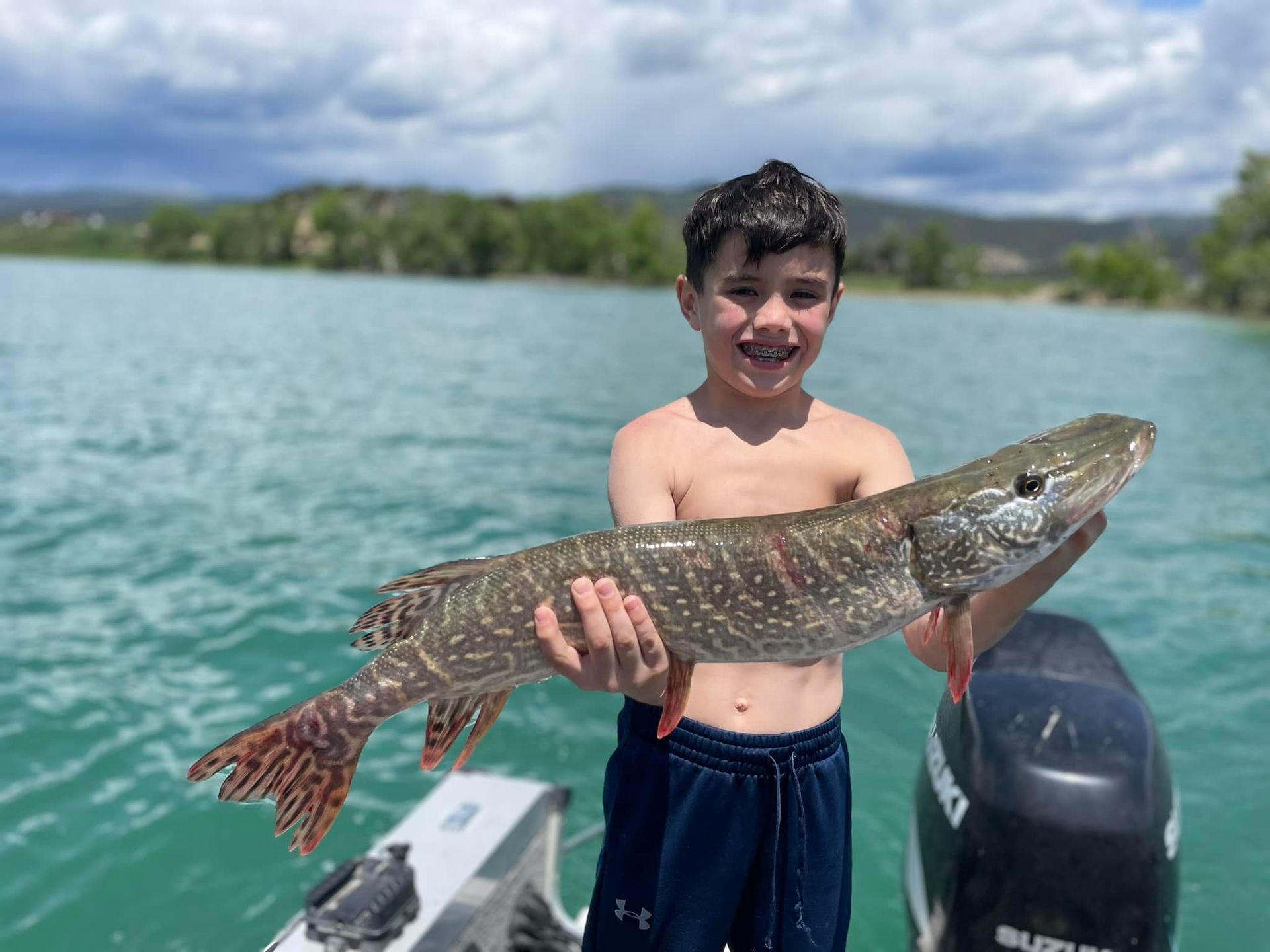 A young boy is holding a large fish on a boat.