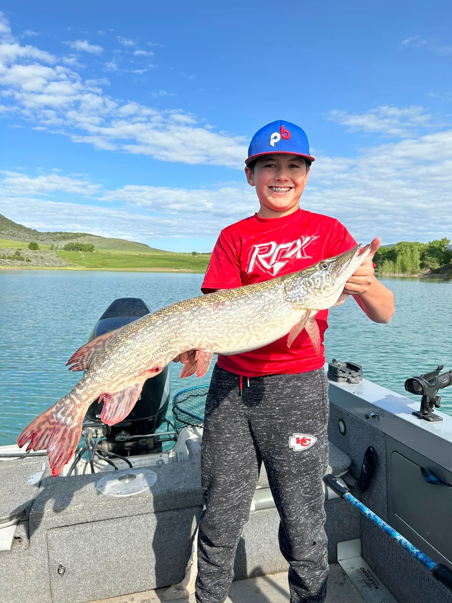 A young boy is standing on a boat holding a large fish.